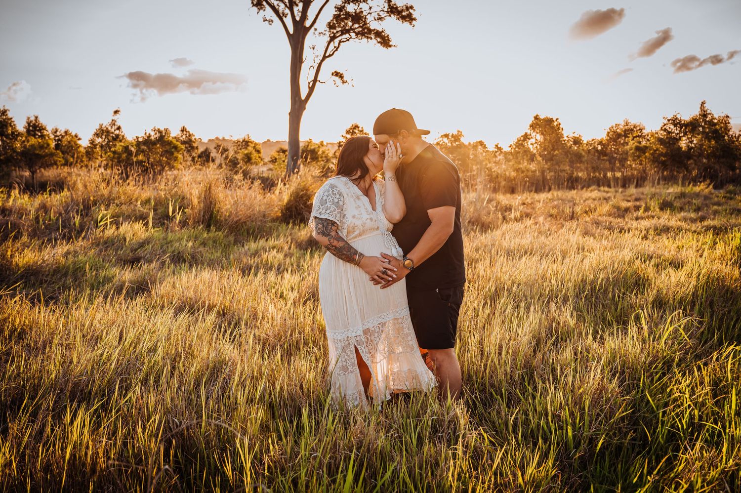 Intimate maternity portrait during golden hour in a grassy field with tall trees.