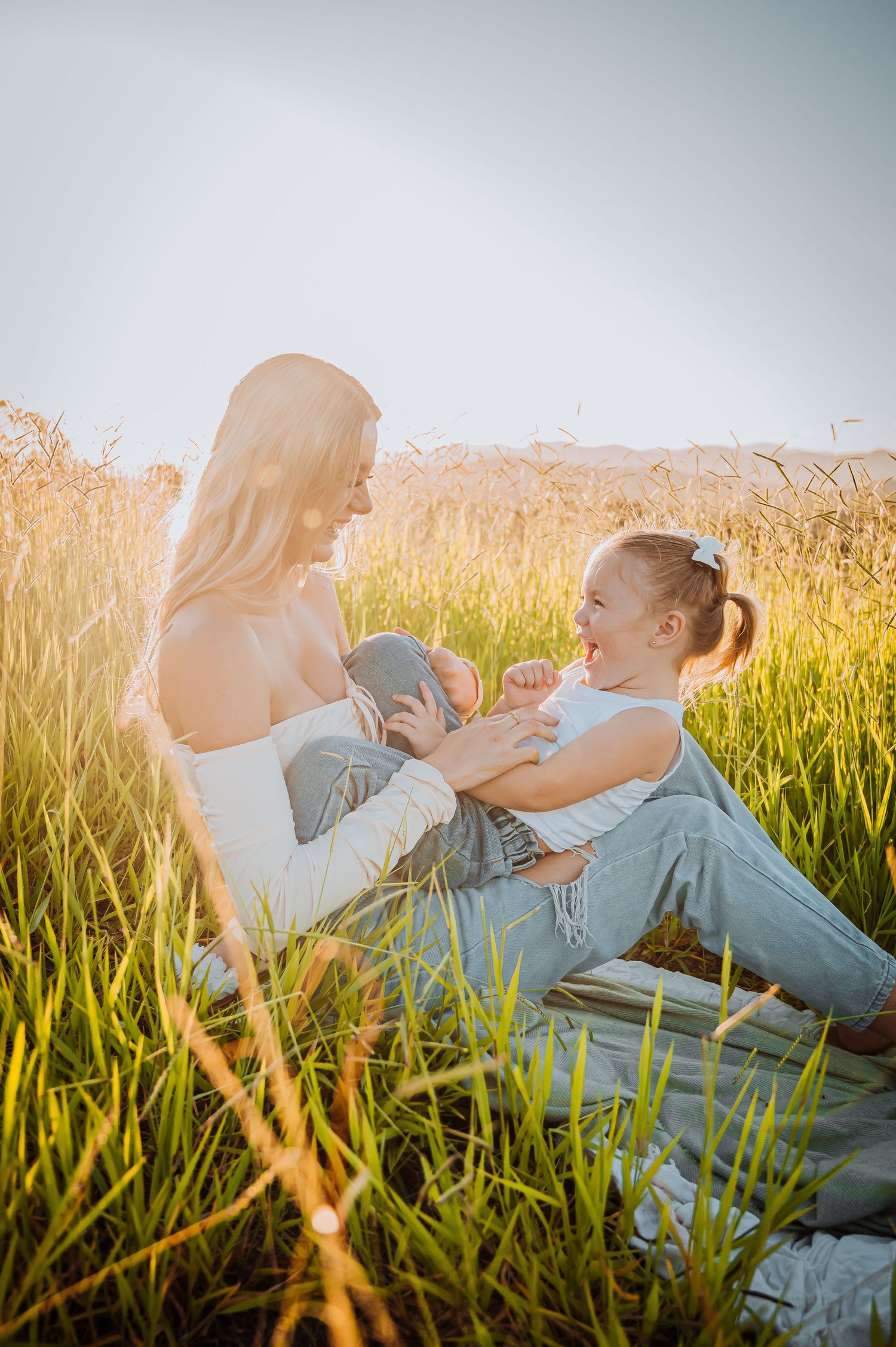 Playful interaction between two people sitting in a sun-drenched field of tall grass.