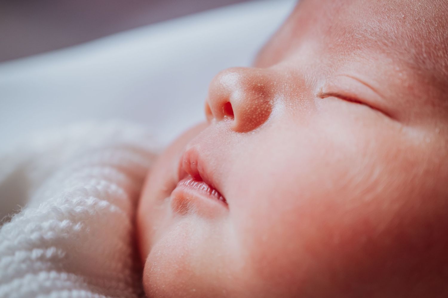 Close-up profile of sleeping newborn baby's face against white fabric.