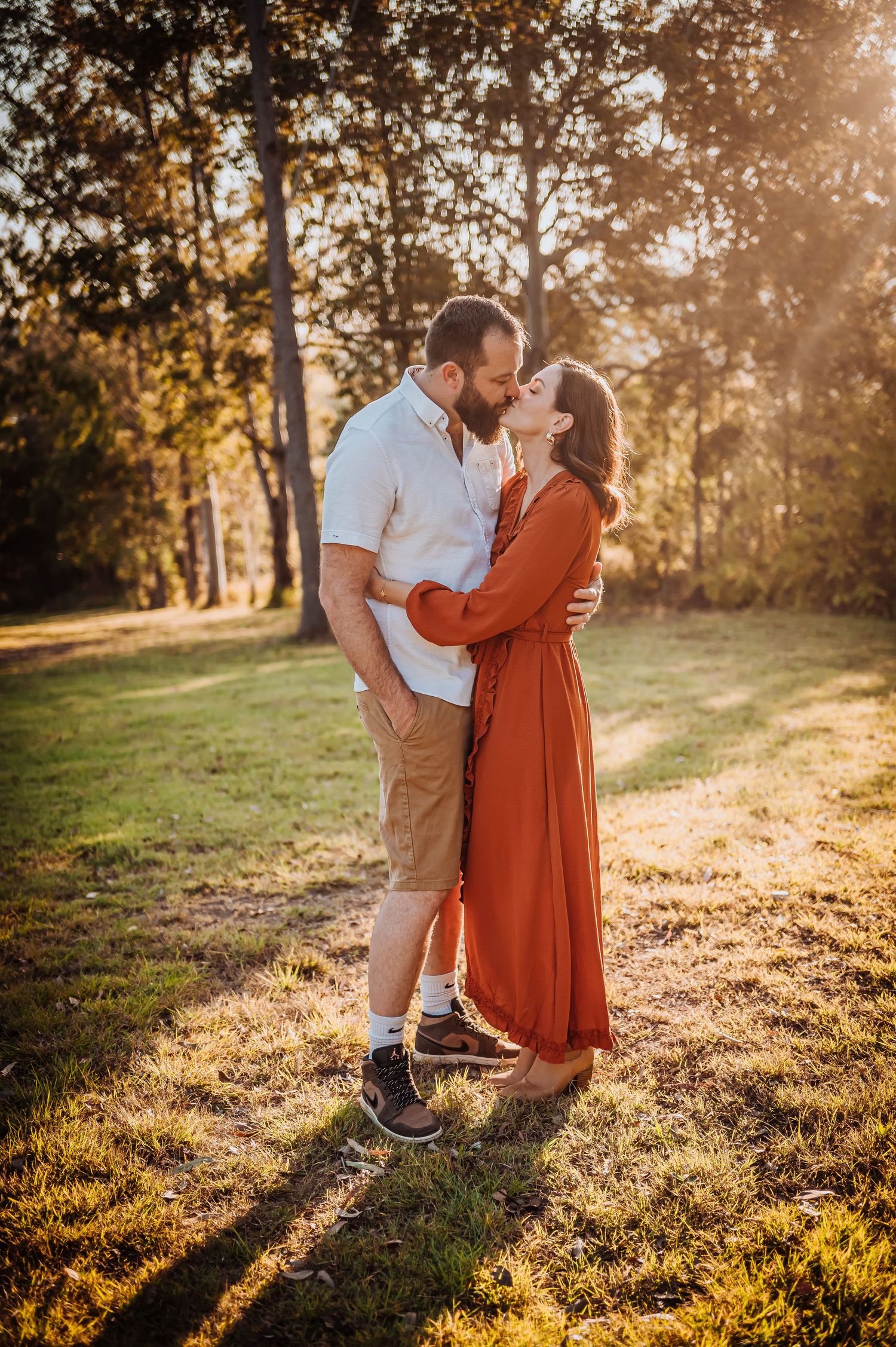 A tender embrace in a sunlit forest clearing during golden hour.