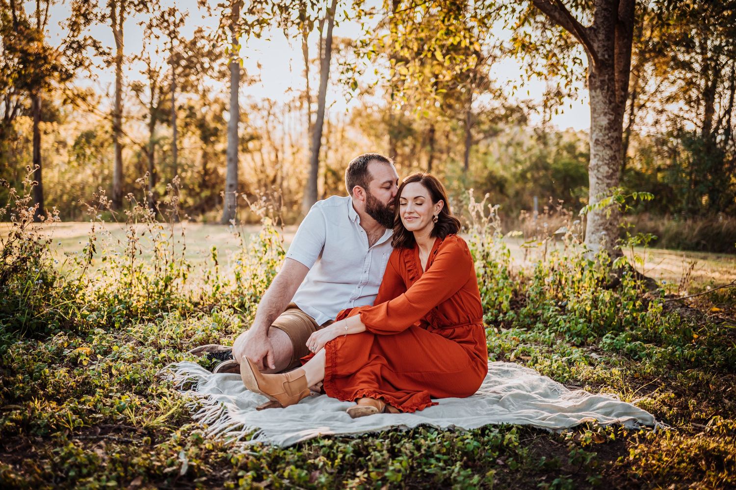 A couple enjoying a picnic on a blanket in a sun-dappled autumn setting.