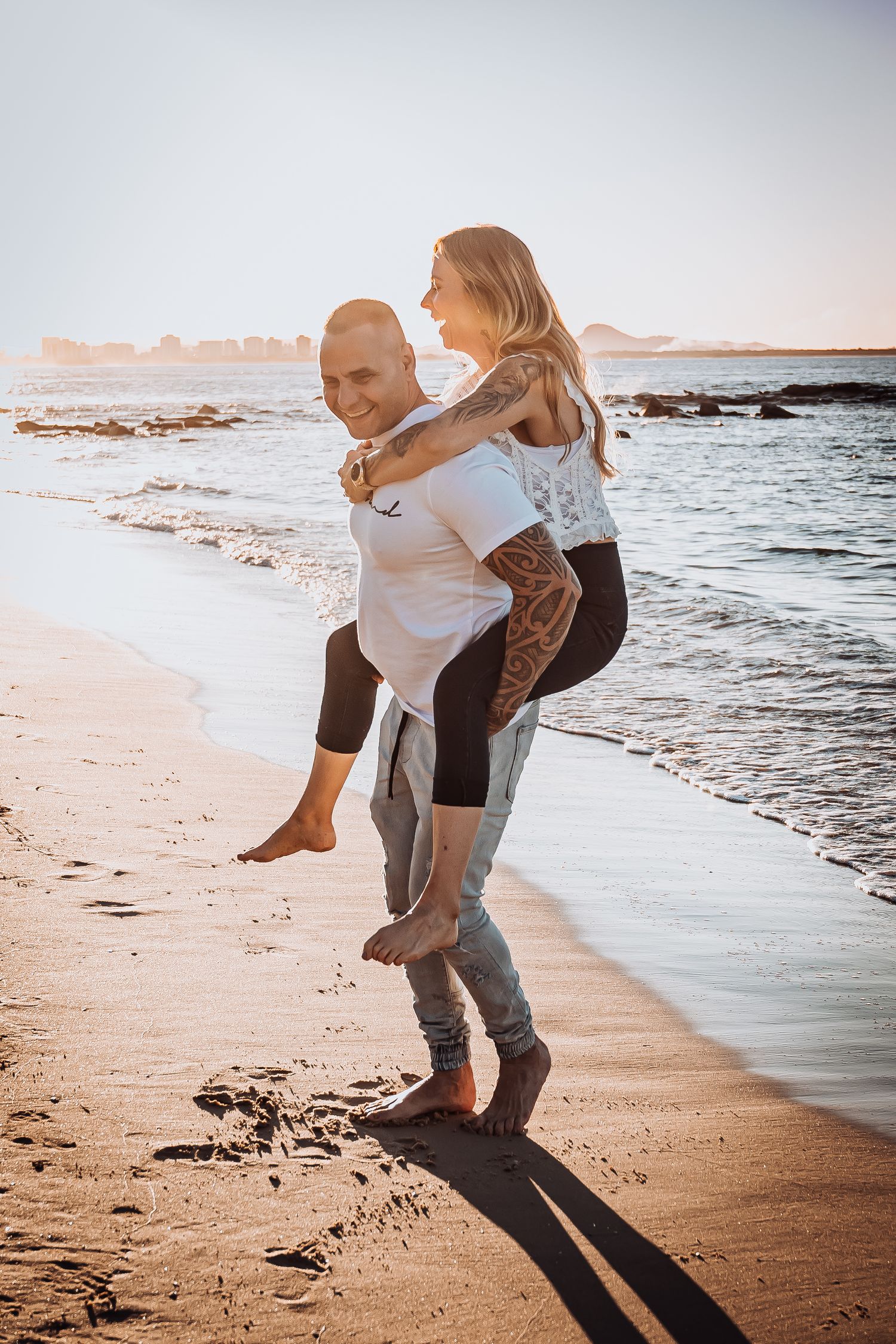 A couple plays and laughs together on a sandy beach at sunset.