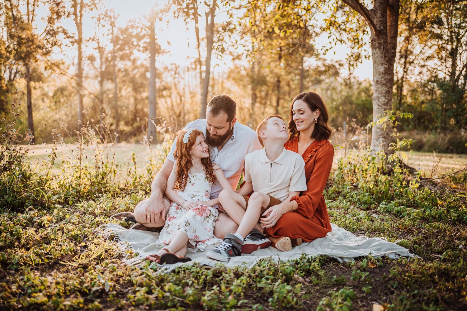 Family relaxing together on blanket in sunlit autumn forest.