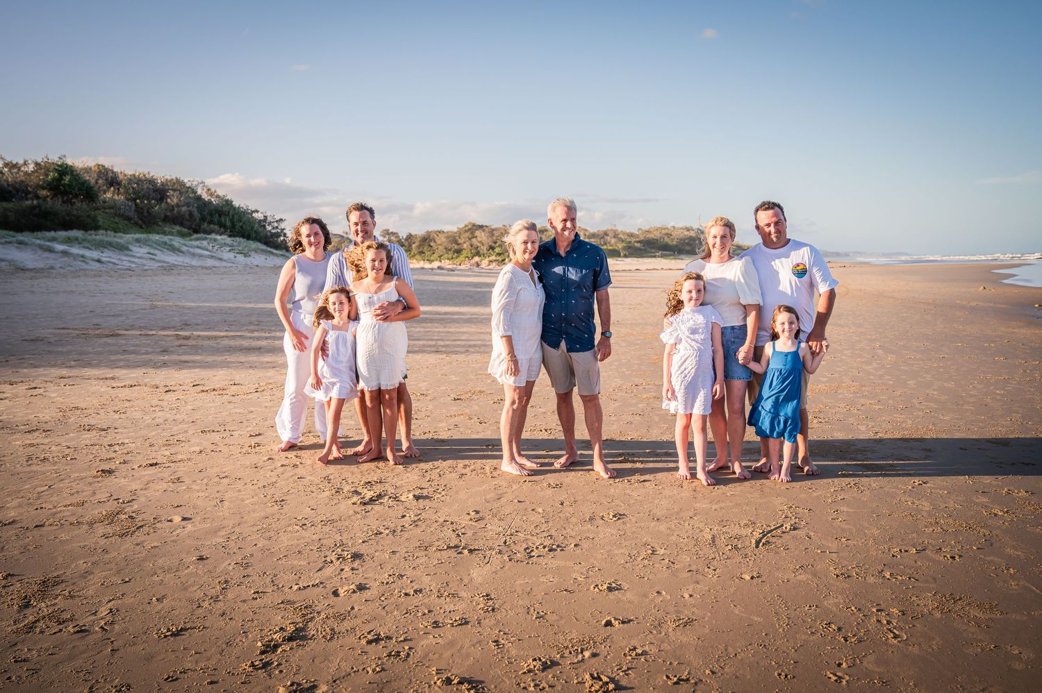 Extended family group poses together for a portrait on a sunny beach.