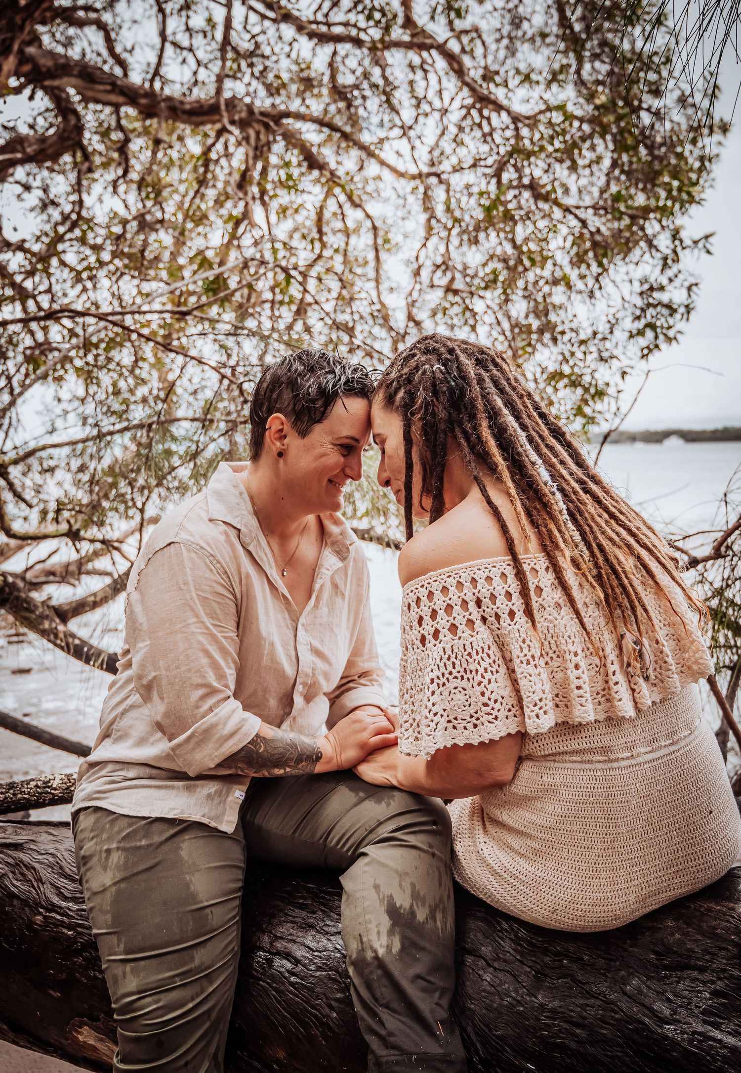 Romantic couple in neutral tones share tender moment while sitting on fallen tree trunk.