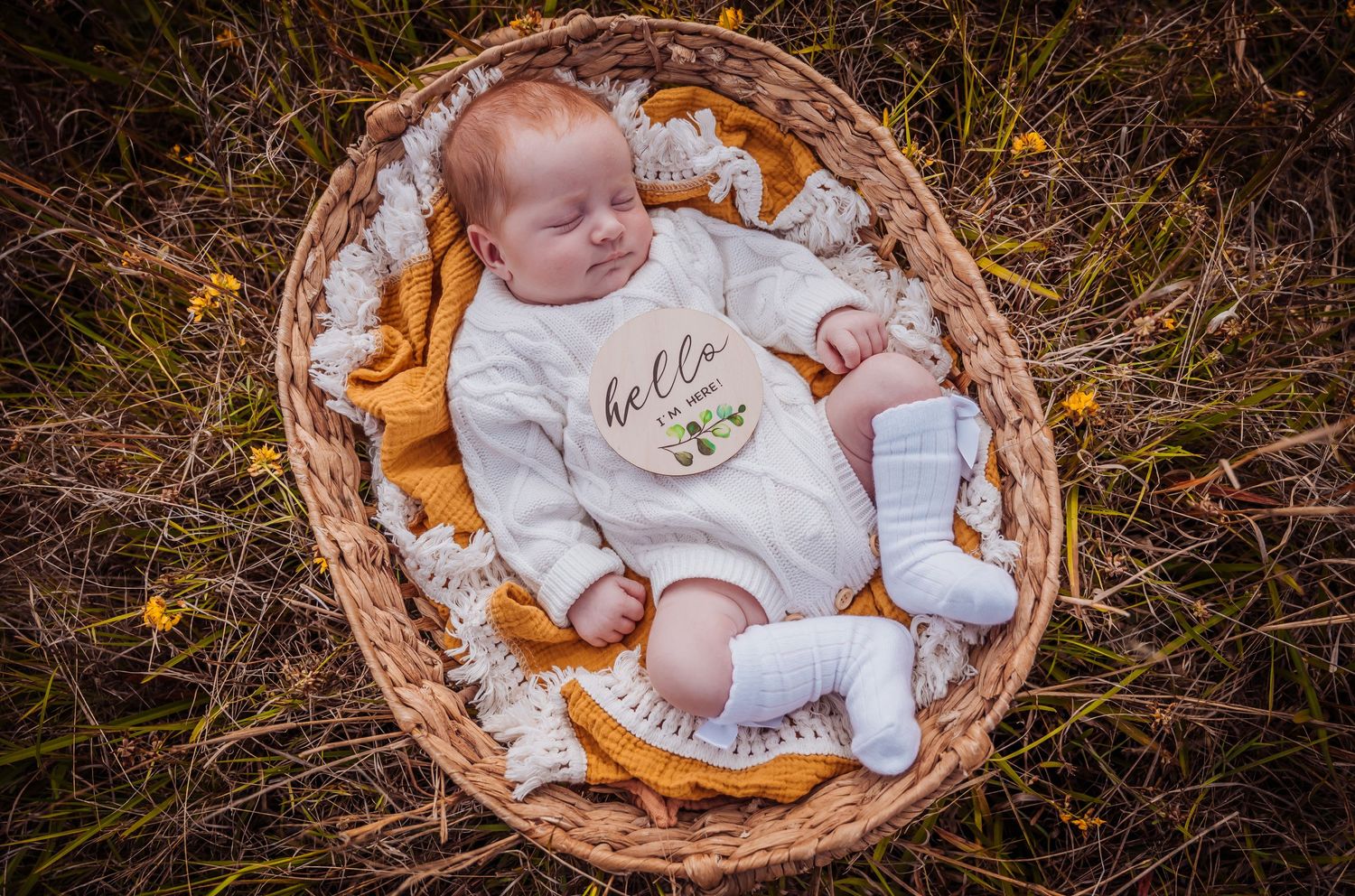 Baby resting in wicker basket with orange blanket outdoors in autumn setting.