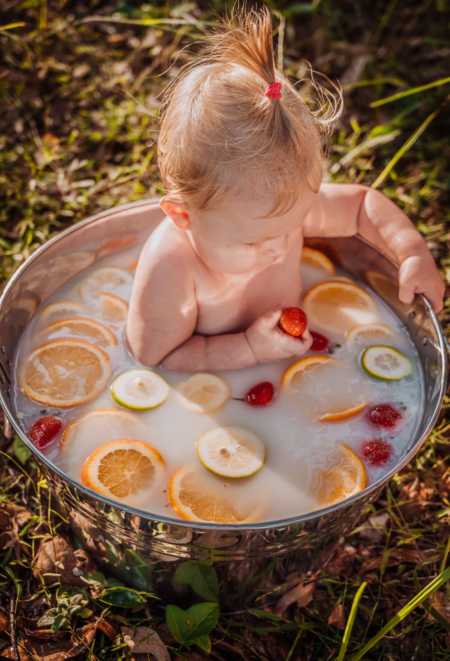 Milk bath photography with citrus slices and flower petals in outdoor setting.