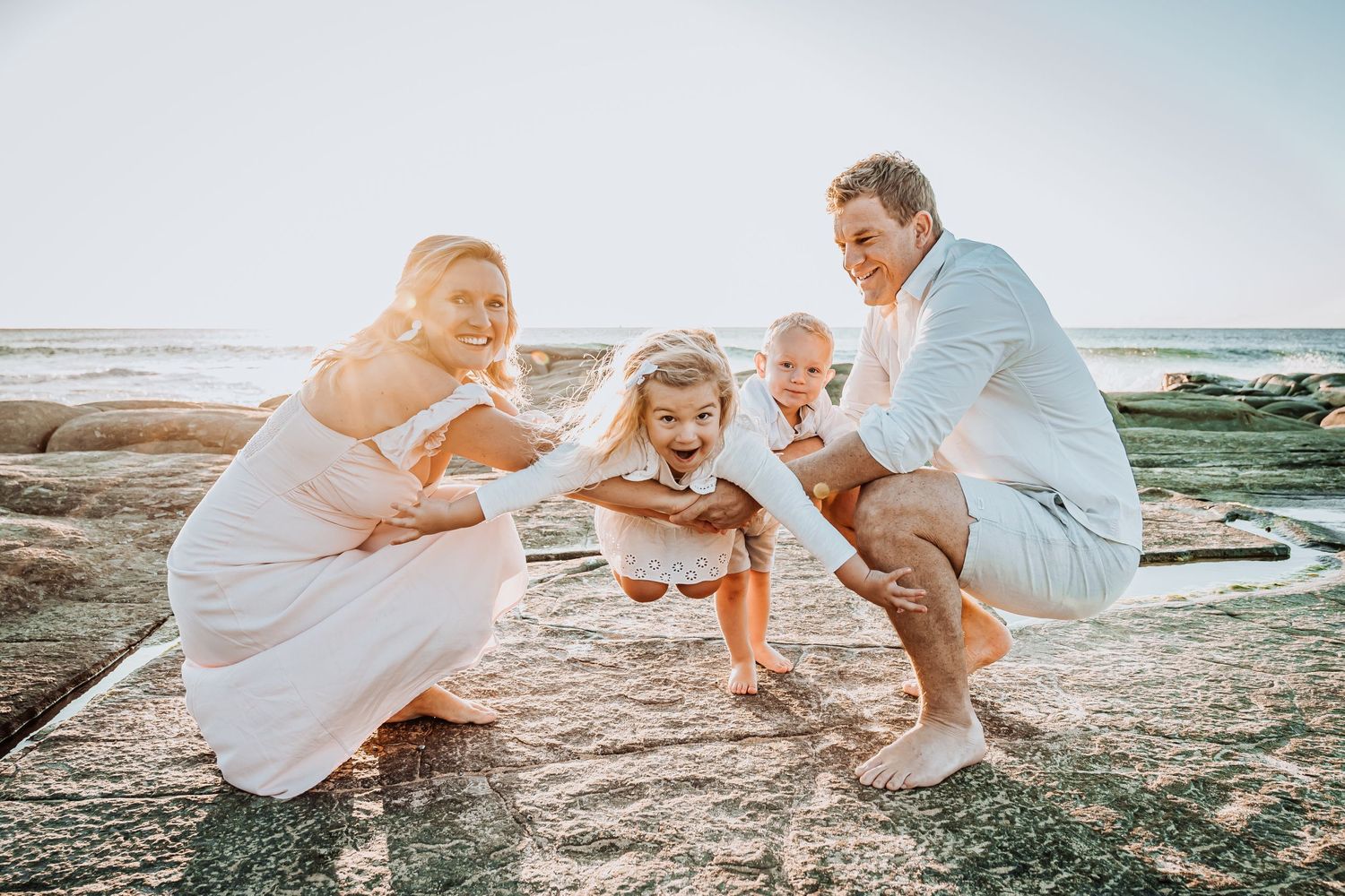 Family enjoying sunset moment together on rocky coastal beach.