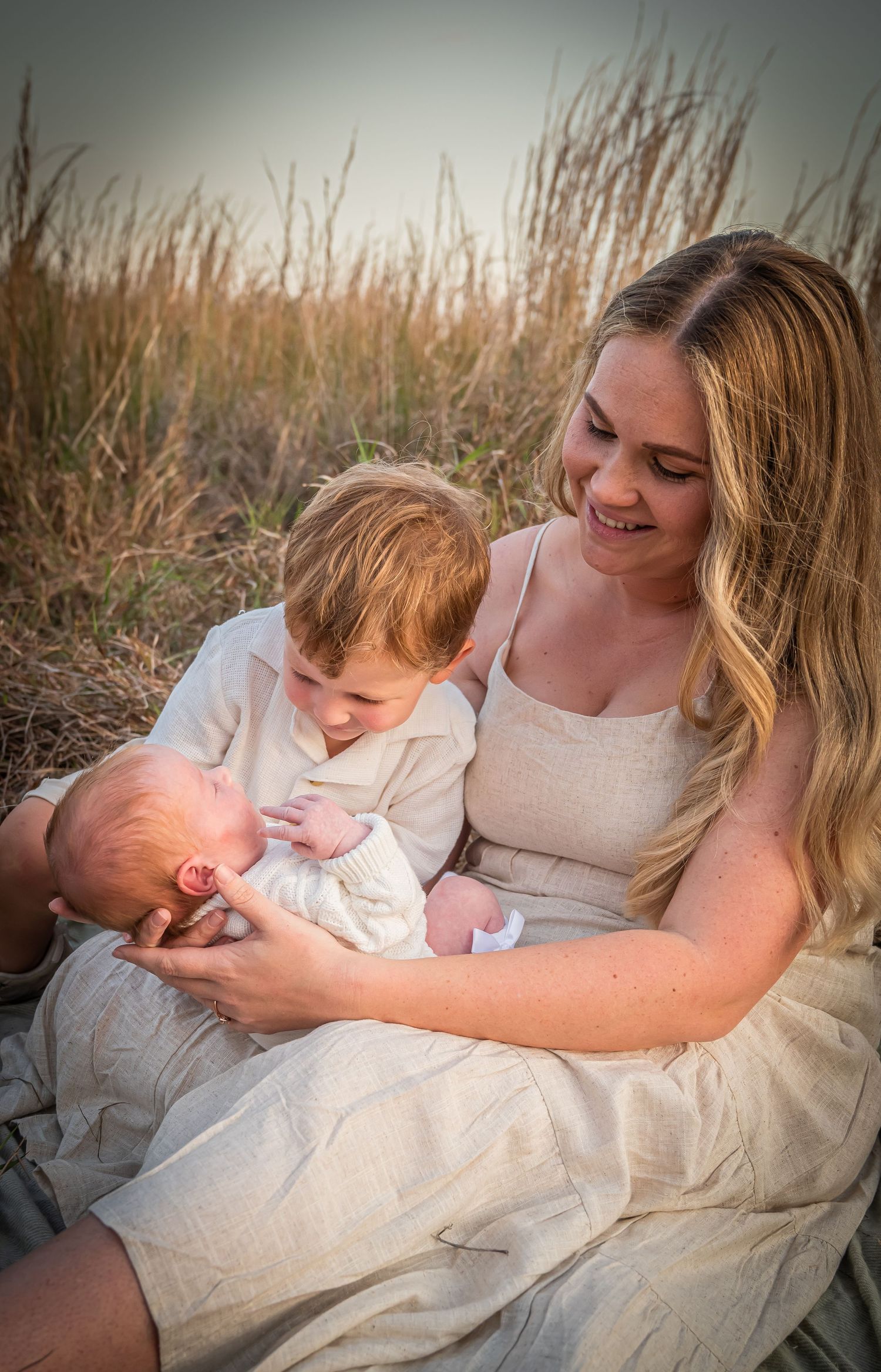 Intimate family moment captured in tall grass during golden hour.