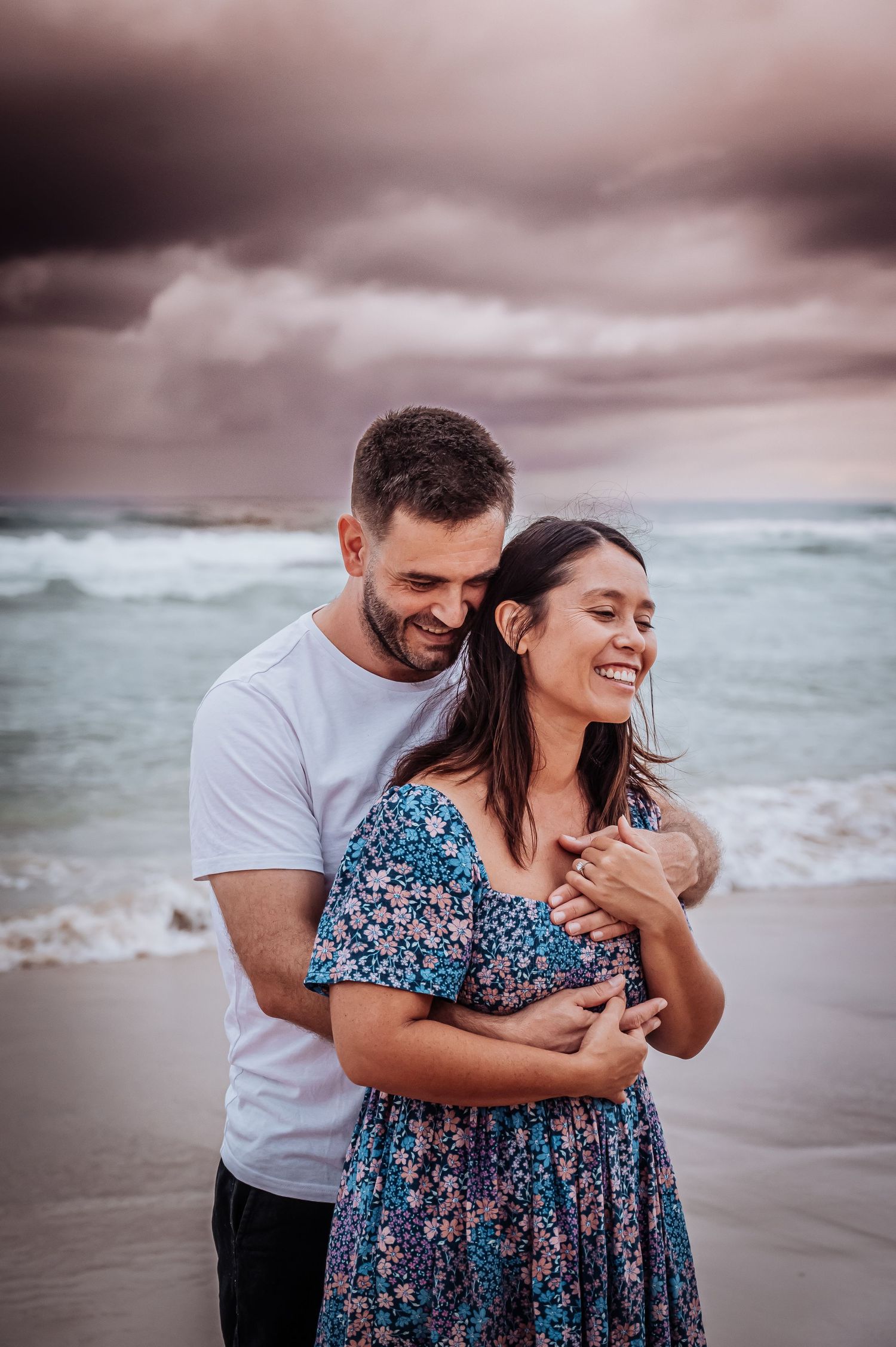 A romantic moment captured on the beach with dramatic stormy skies overhead.