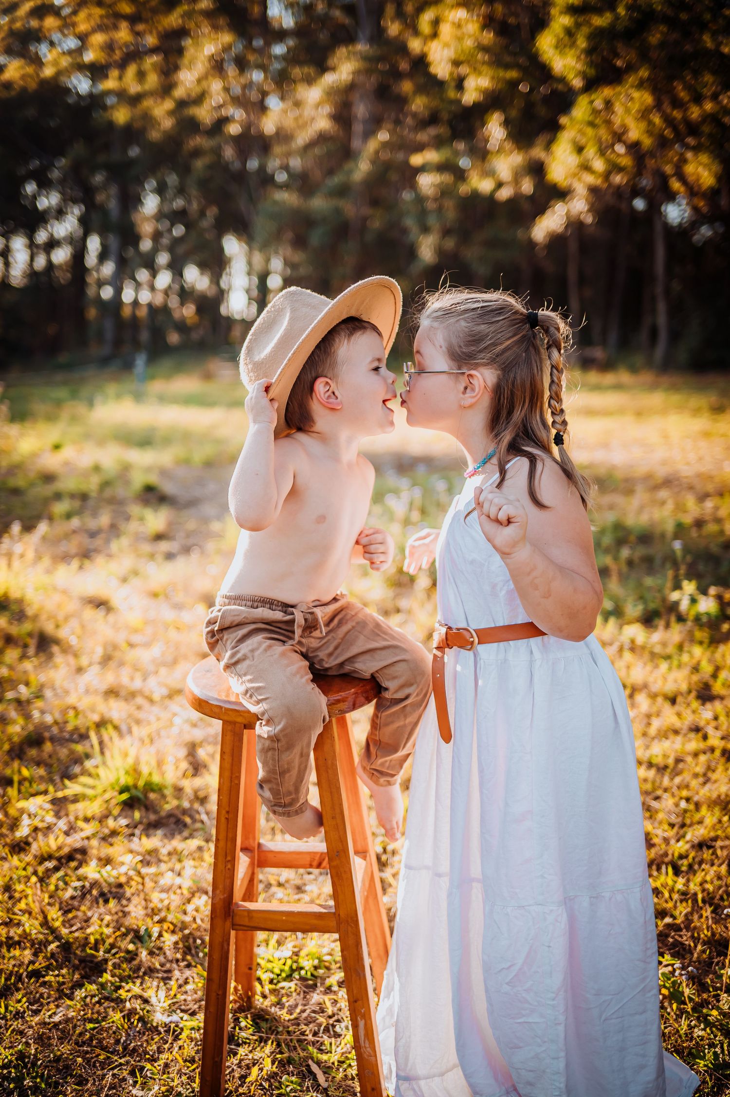 Two children share tender moment on wooden stool in golden autumn sunlight.