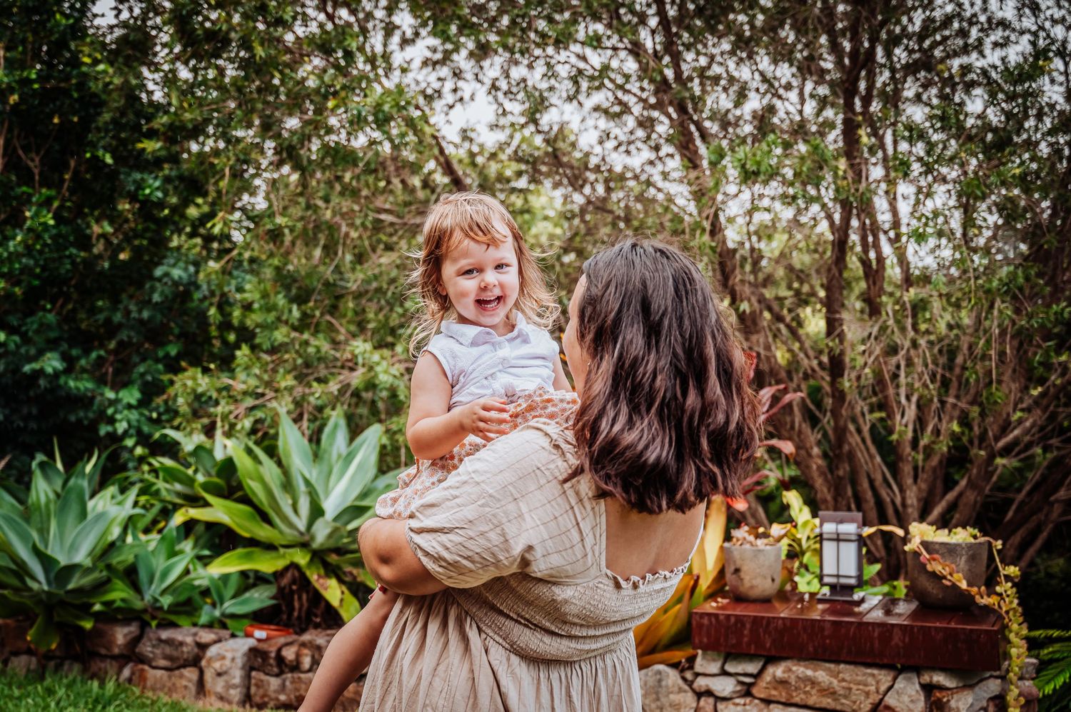 A playful interaction between parent and child in a lush garden setting with warm lighting.