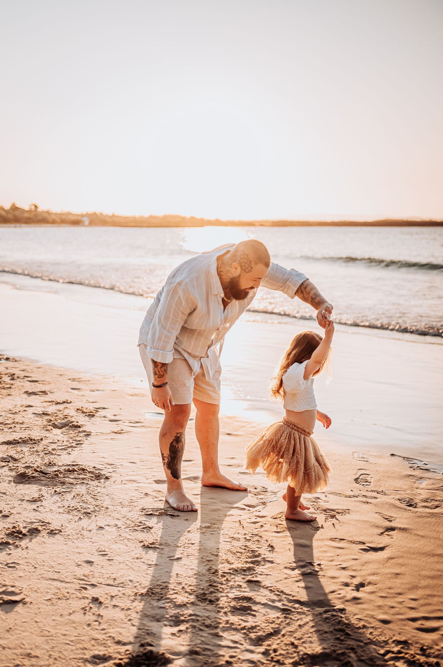 Dancing together on sandy beach at sunset with ocean waves in background.