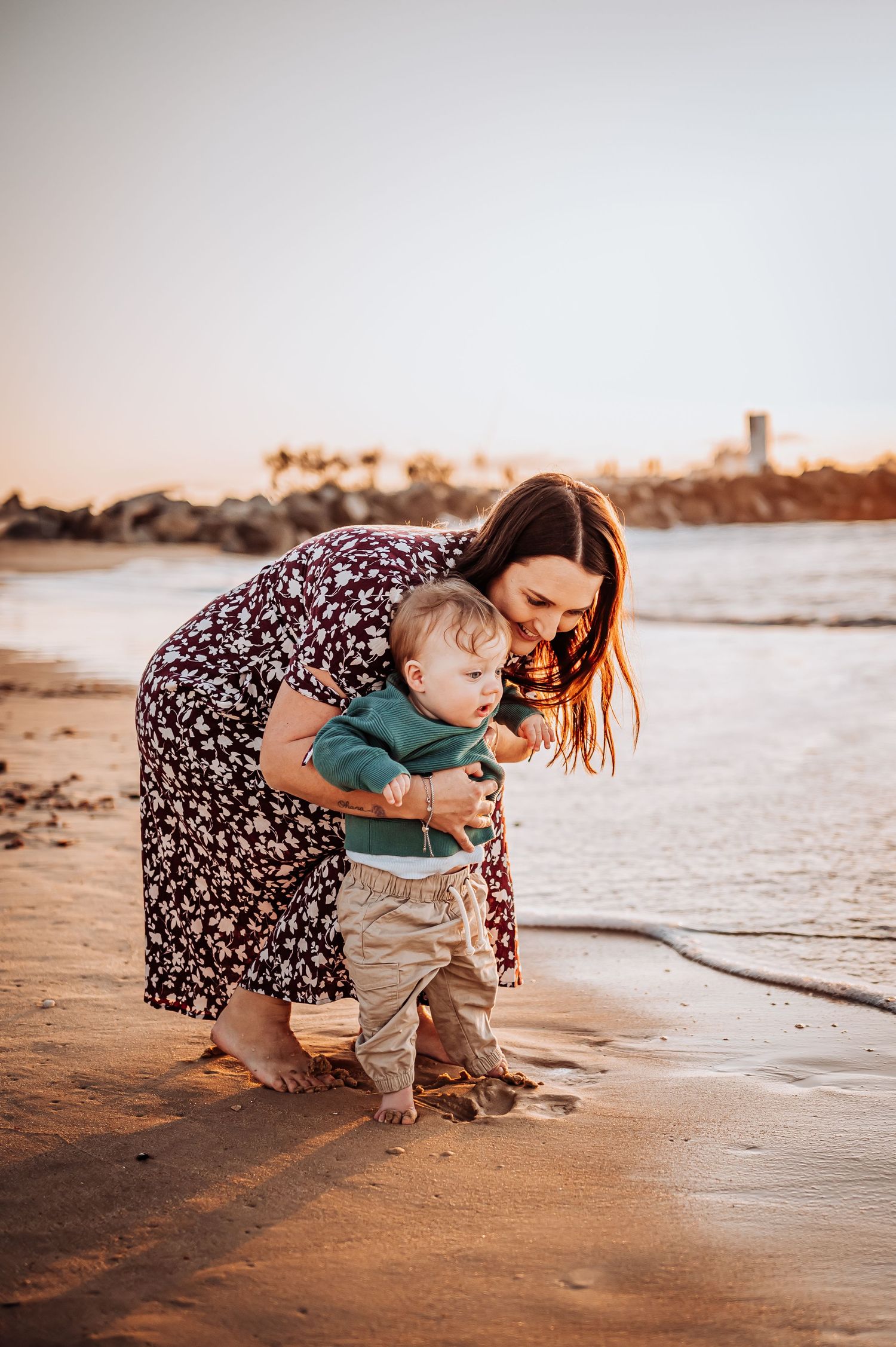 Parent and toddler exploring beach together at sunset.