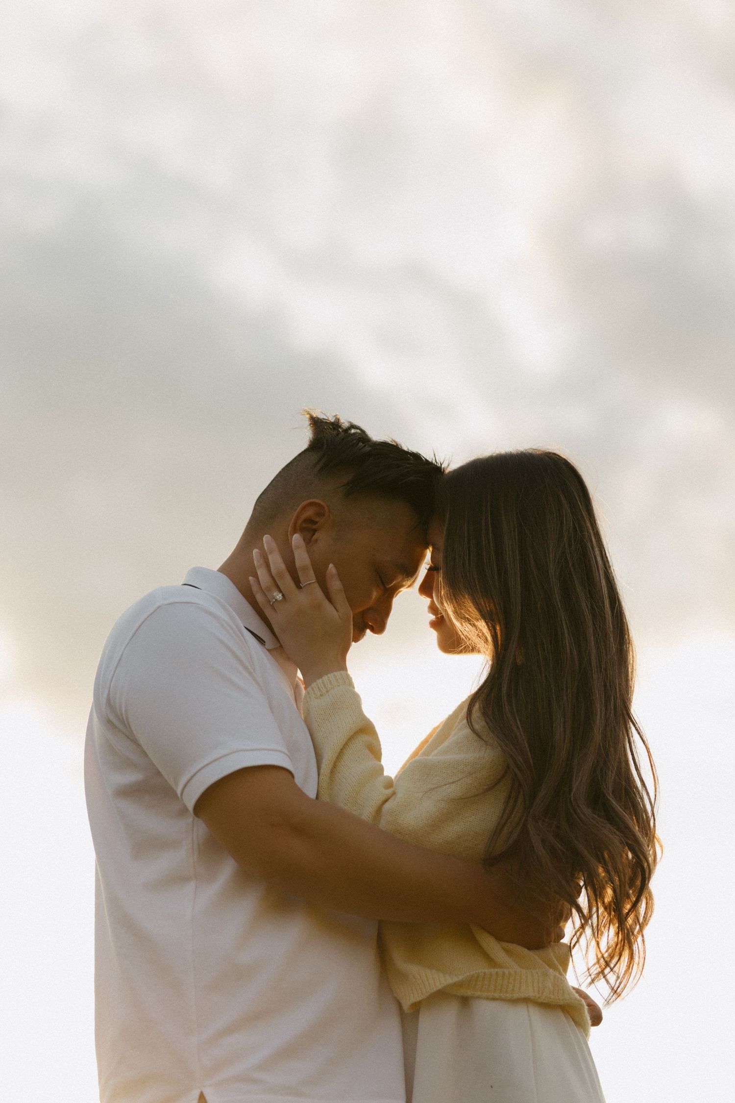 Romantic couple sharing an intimate moment, touching foreheads against a dramatic cloudy sky at sunset.