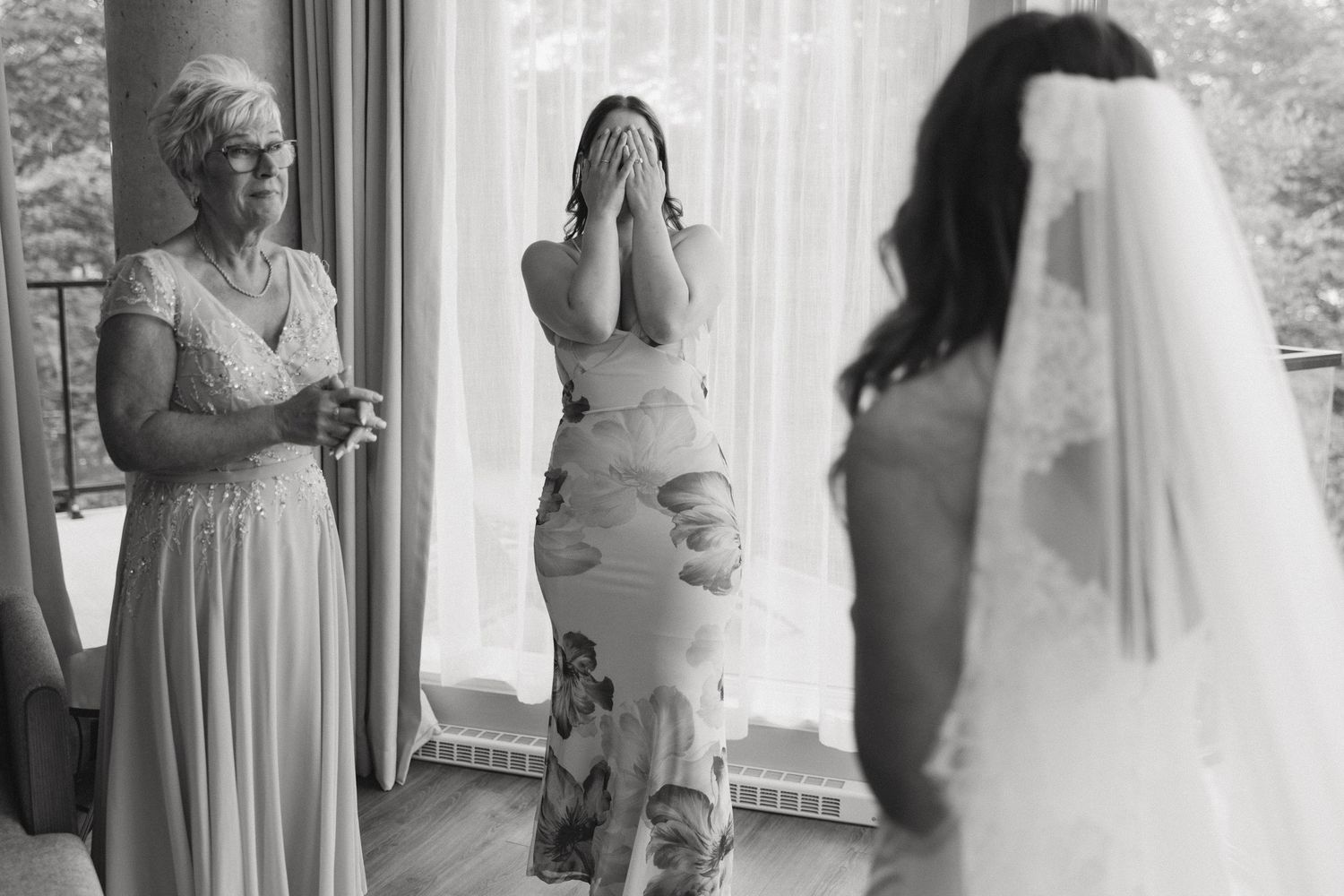 Bride in veil surprises emotional family members, woman covering face in tears during wedding dress reveal.