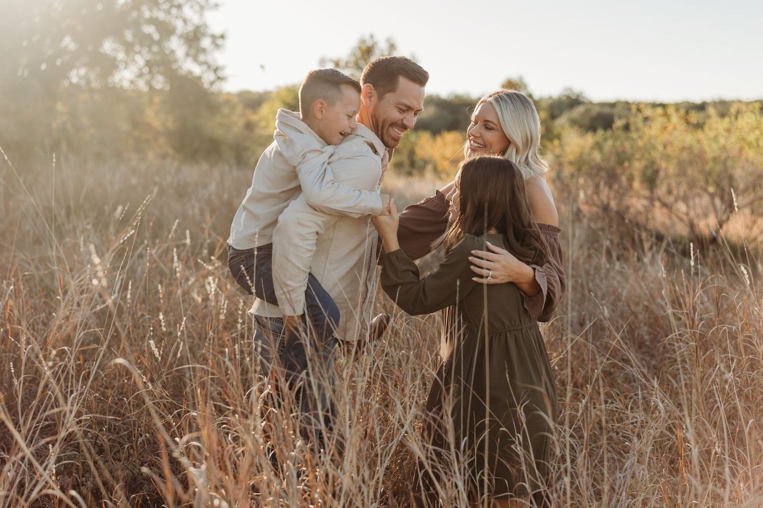 Family of four sharing a joyful moment together in a golden field at sunset.