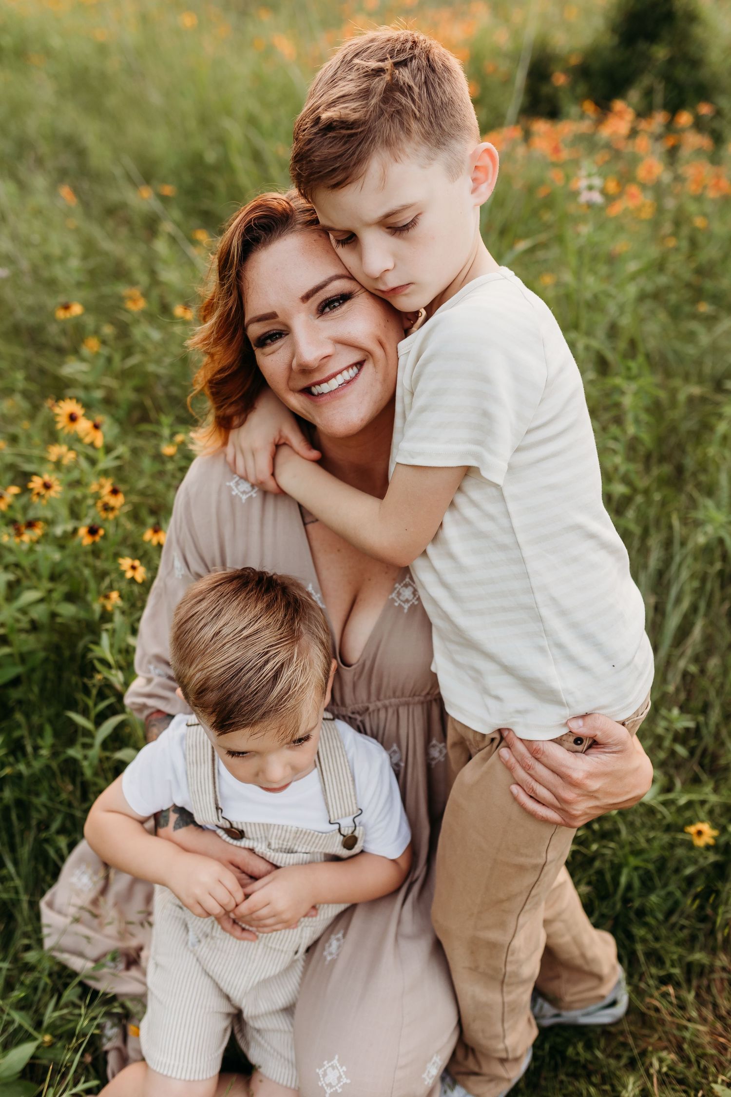 A smiling mother is embraced by her two young sons in a field of wildflowers.