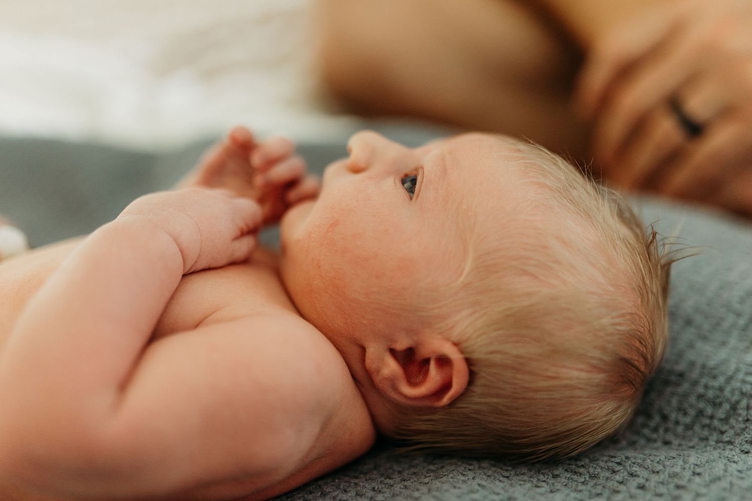 Close-up of a peaceful newborn baby lying on a soft blue blanket with tiny hands raised.