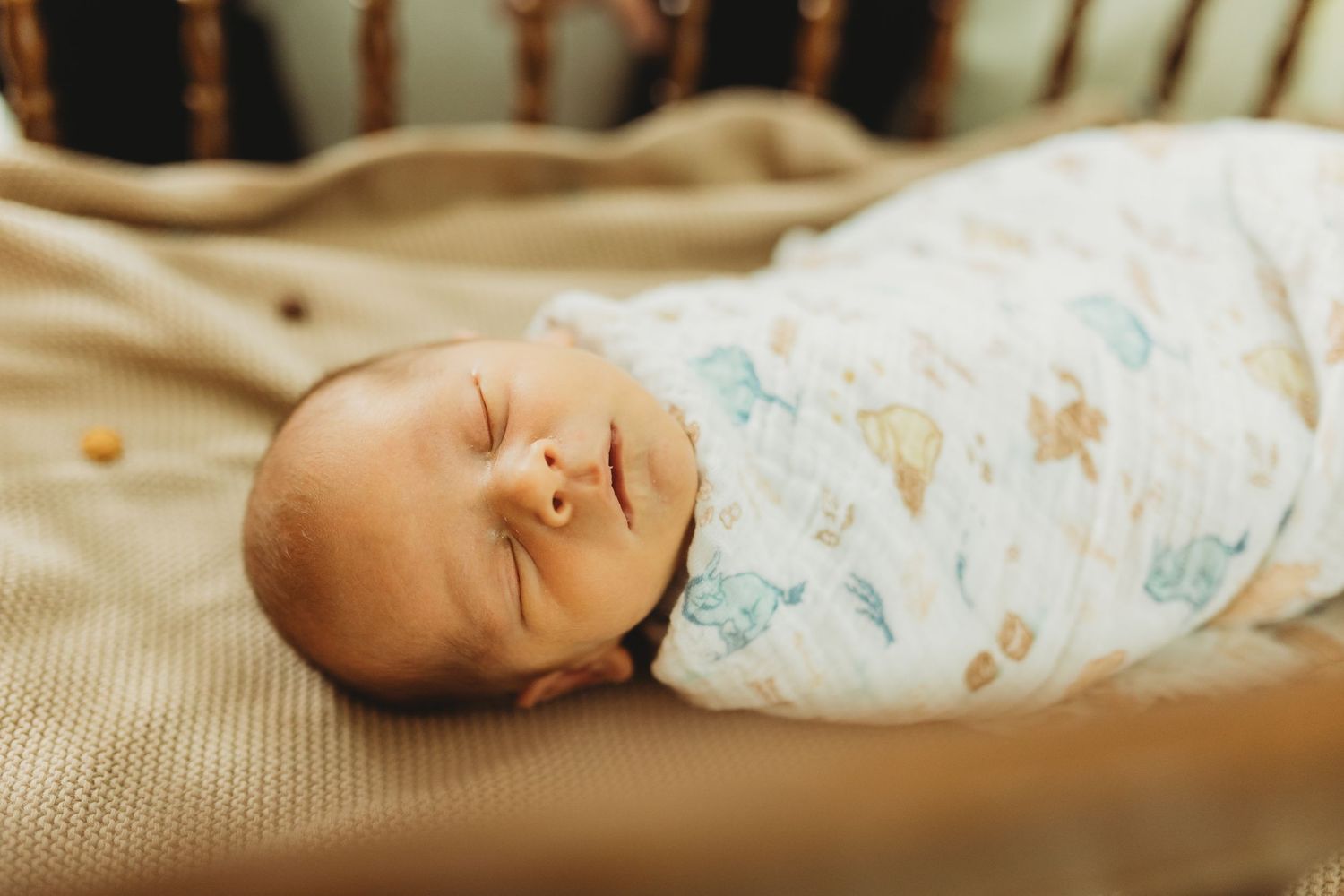 Peaceful newborn baby swaddled in white floral blanket sleeping in wooden crib.