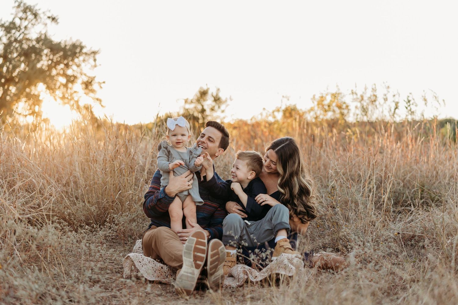 Joyful family sitting together in tall golden grass during a warm sunset outdoor photo shoot.