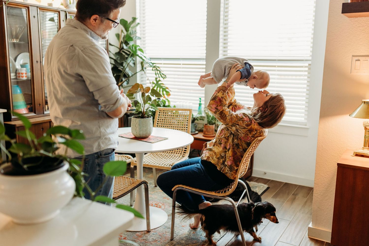 Parents playing with baby indoors, mother lifting child joyfully in cozy home.