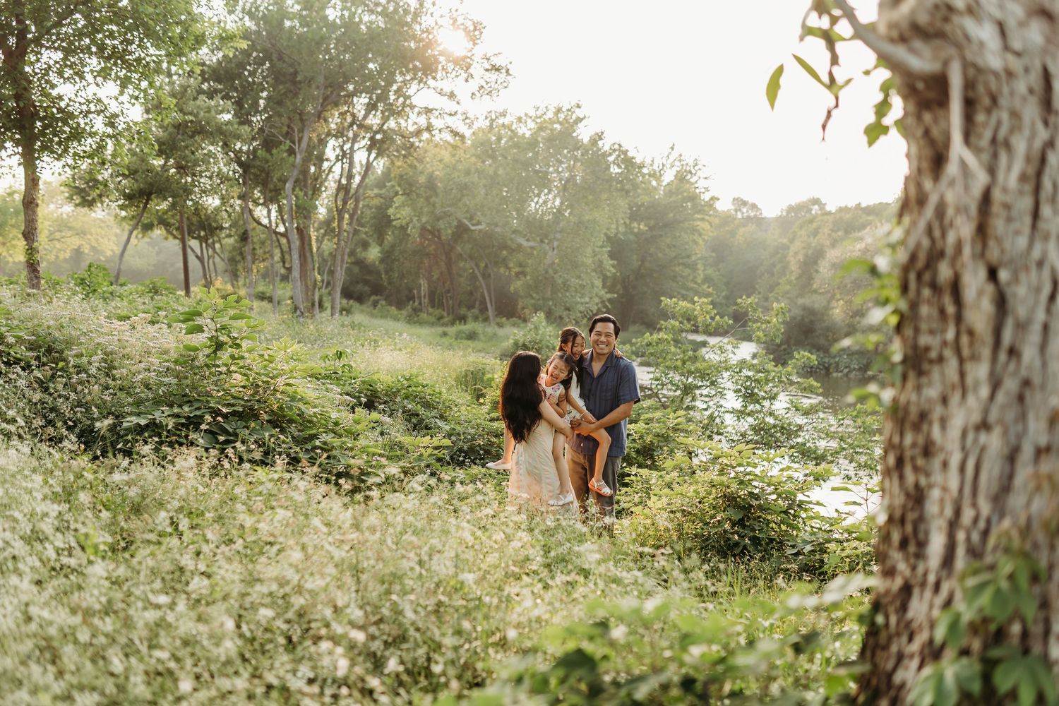 Happy family with child enjoying golden hour near a peaceful creek surrounded by greenery.