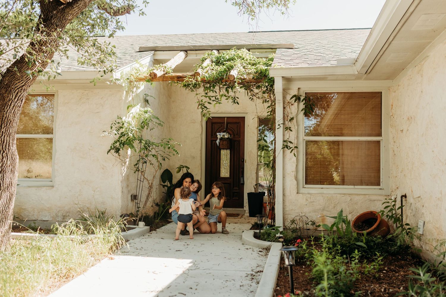 A mother and young child sit together on the front steps of a charming vine-covered home.