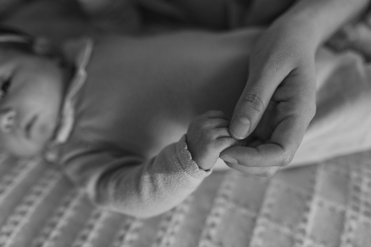 A black and white close-up of a parent's hand gently holding a newborn baby's tiny feet on a soft blanket.