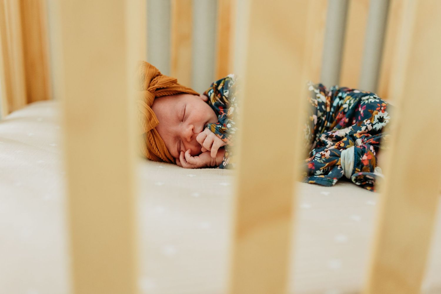 A sleeping newborn baby with an orange bow lies in a wooden crib.