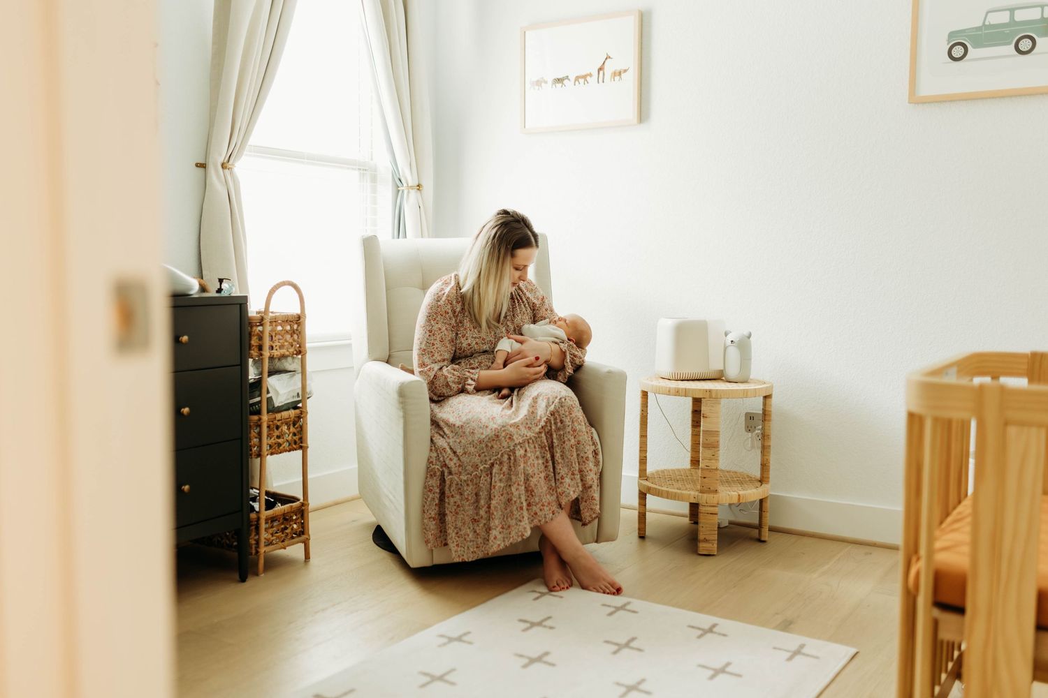 Mother sitting in nursery glider chair breastfeeding newborn baby in softly lit room.