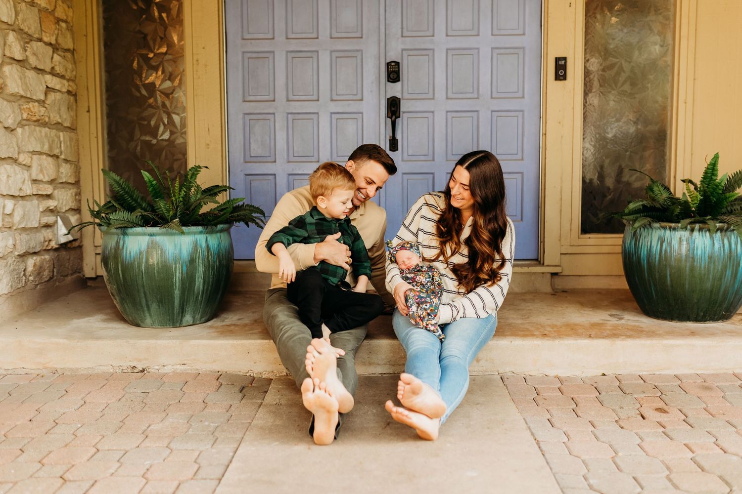 Young family sitting on front porch steps with two children in front of a blue door.
