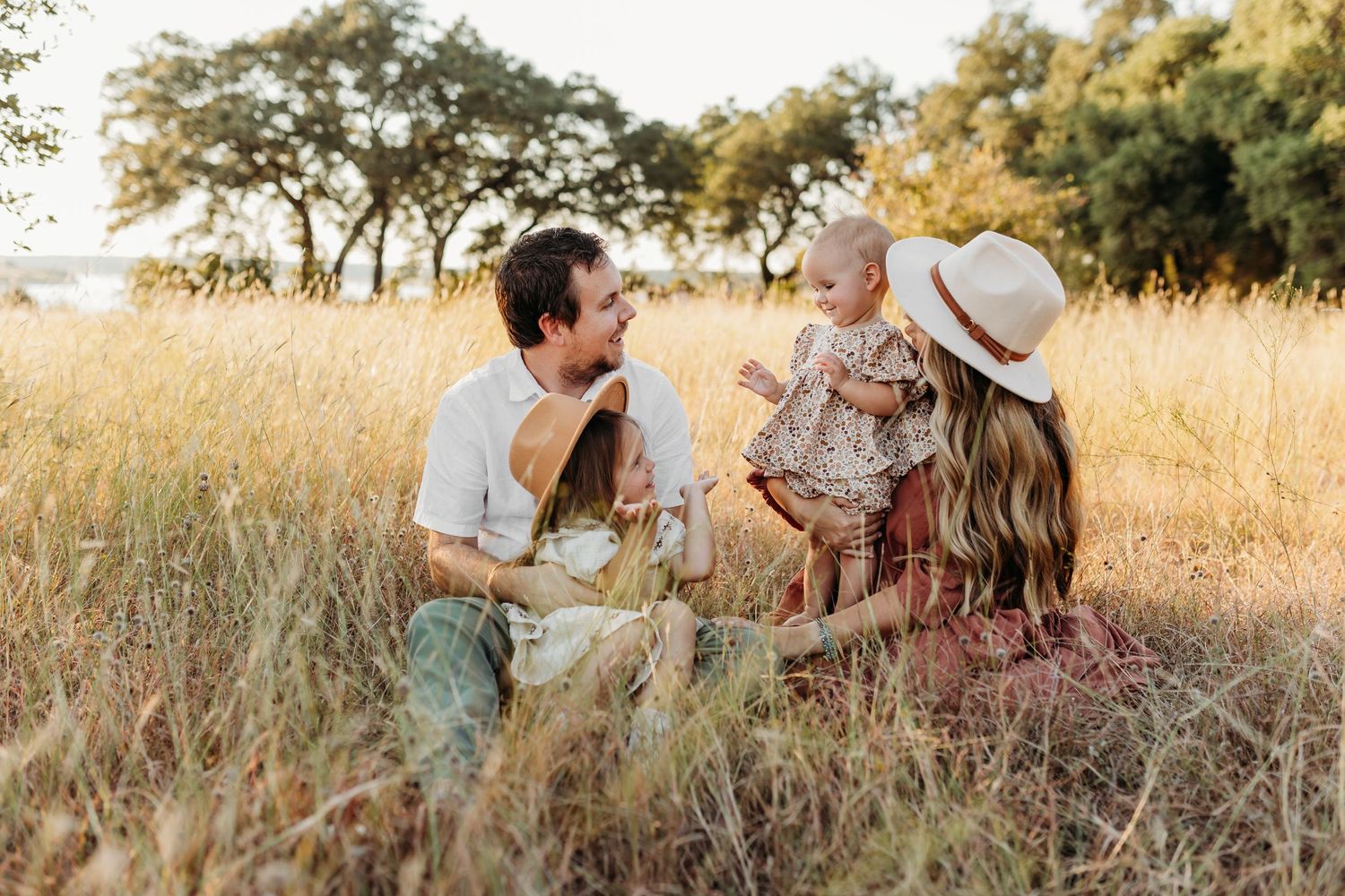 Happy family sitting in tall golden grass field enjoying sunny outdoor session.