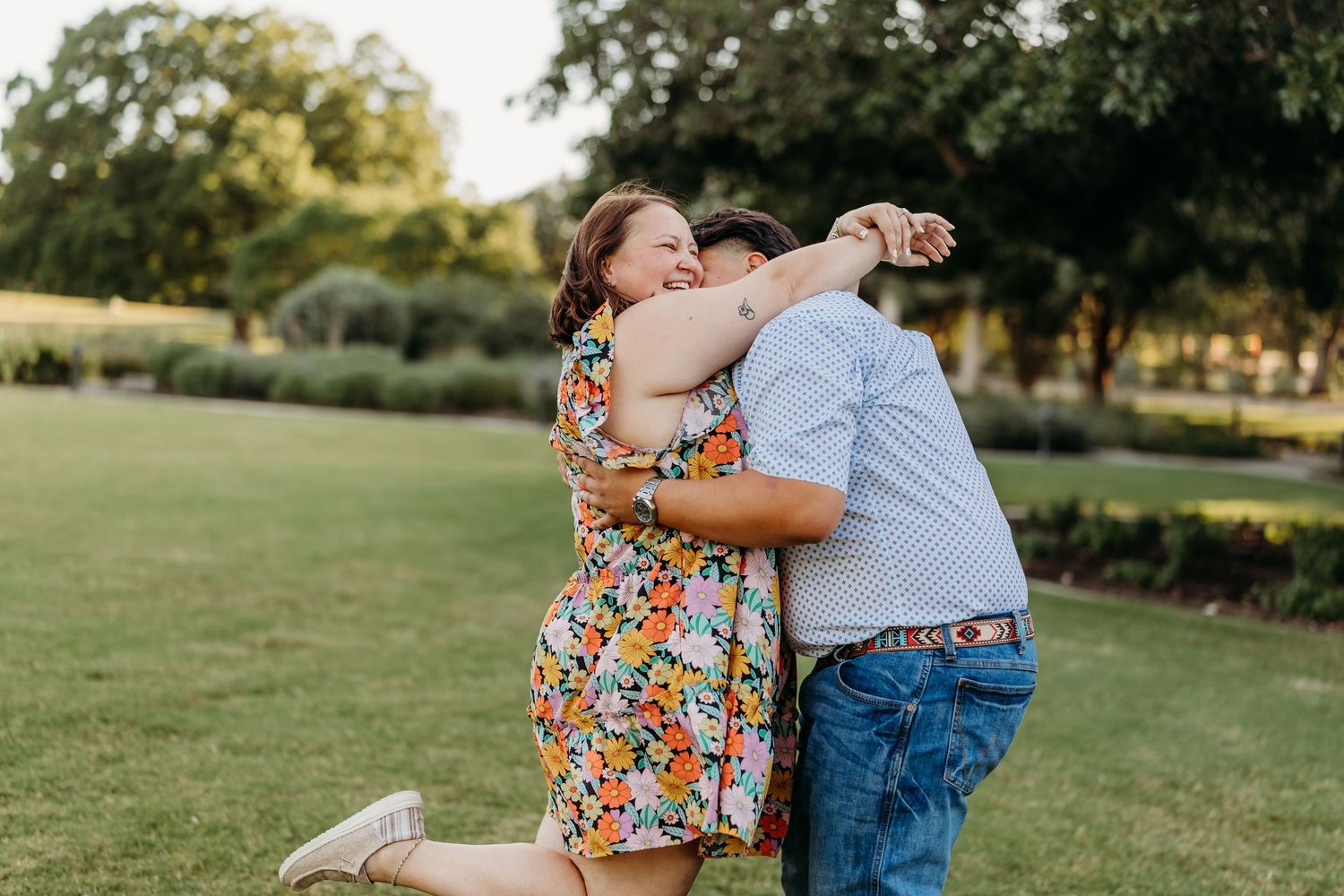 Woman in floral dress hugging a boy on a green lawn outdoors.