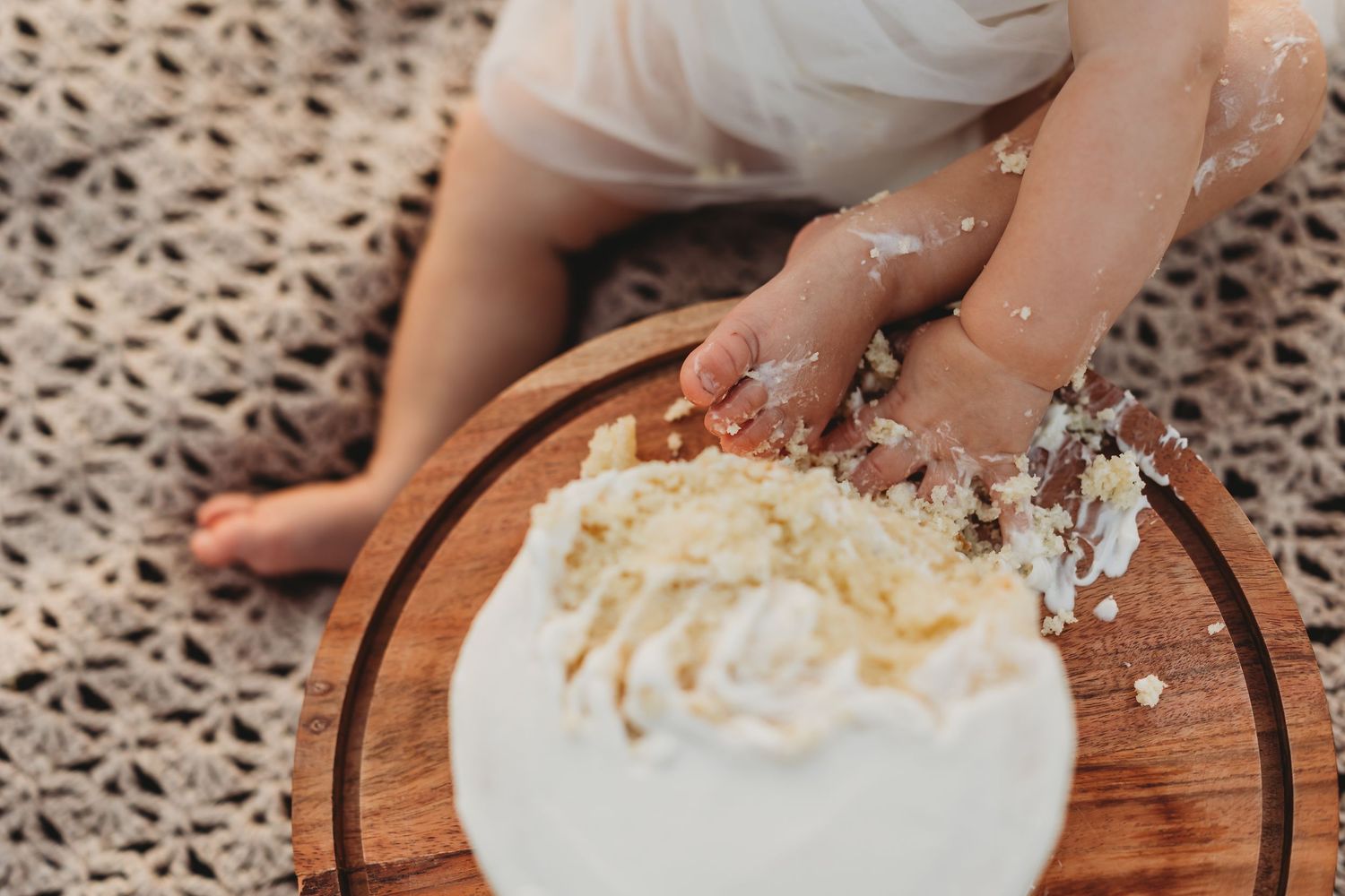 Baby hands smashing a white first birthday cake on a wooden board.