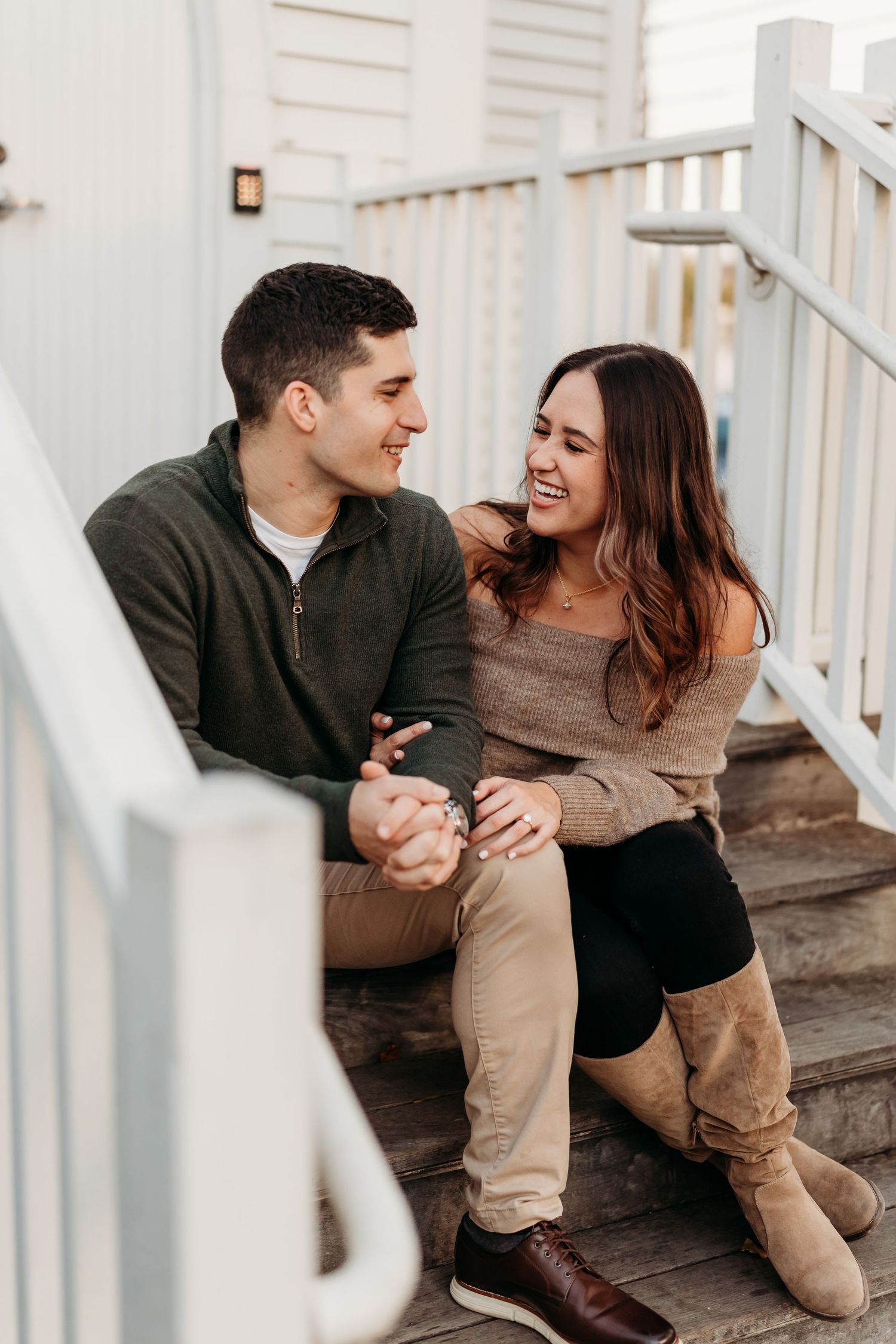 Happy couple sitting on wooden porch steps holding hands and smiling at each other in fall.