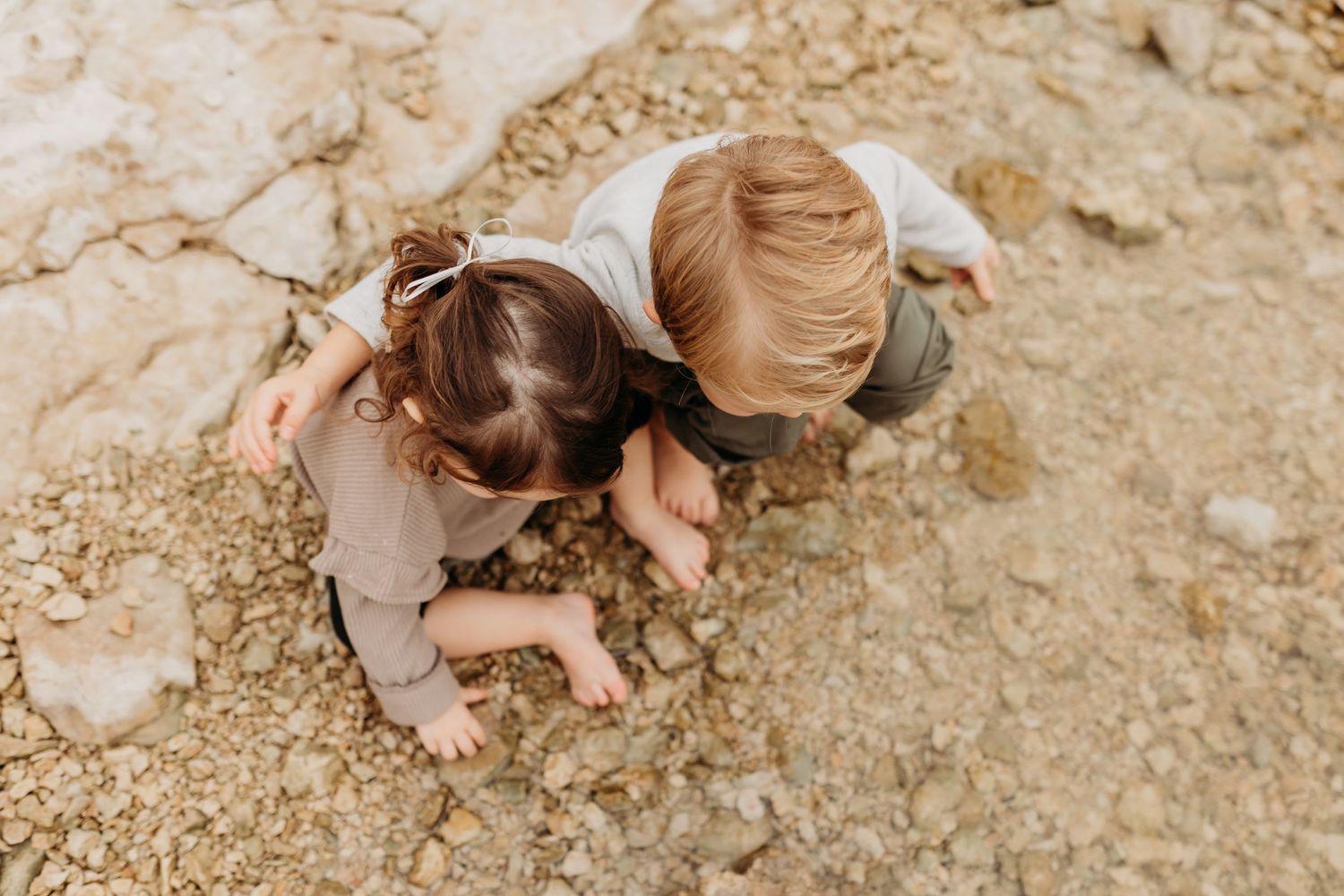 Two young children crouching together exploring rocky ground from an overhead perspective.