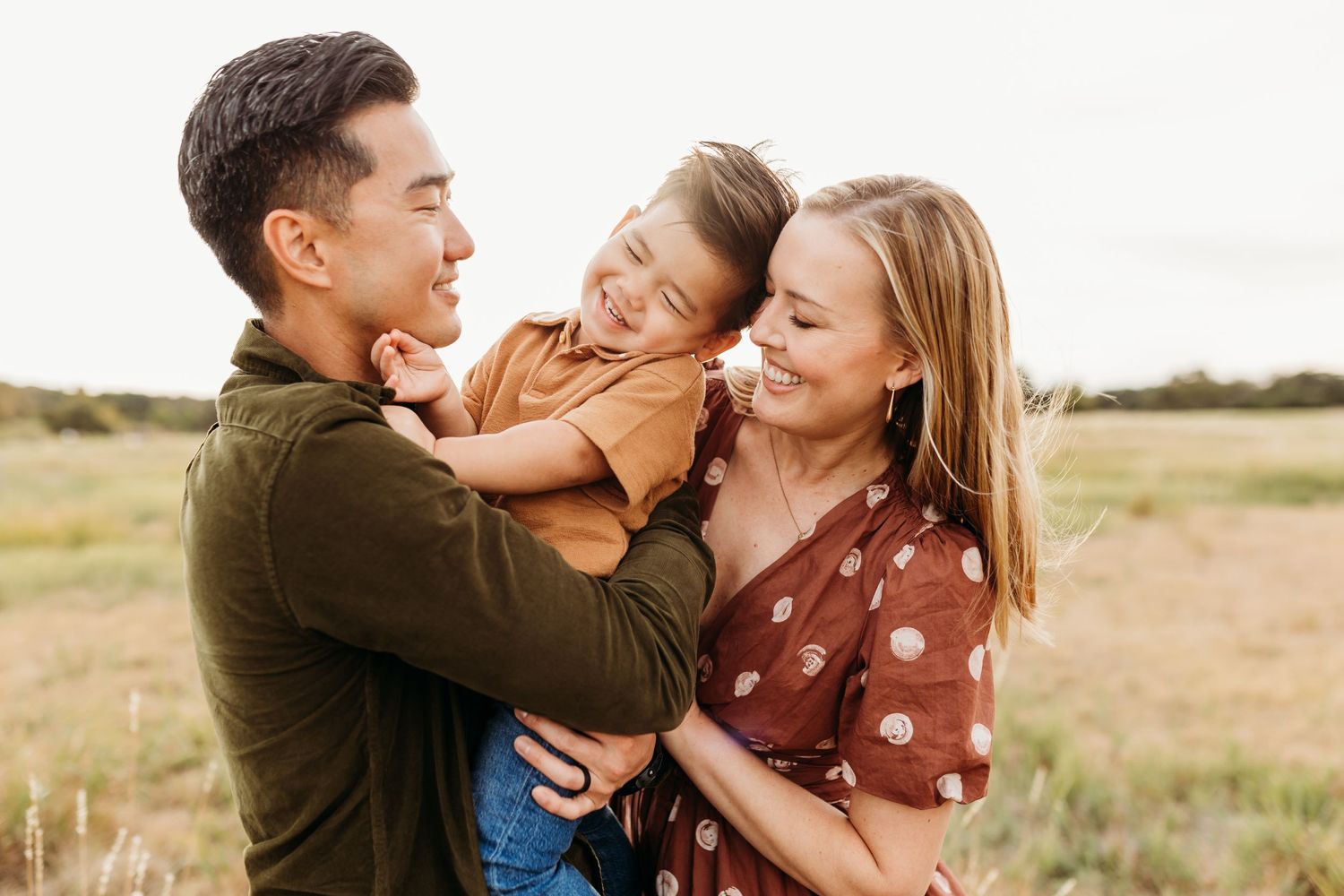 Two parents lovingly embrace their young child between them during a warm outdoor family portrait session.