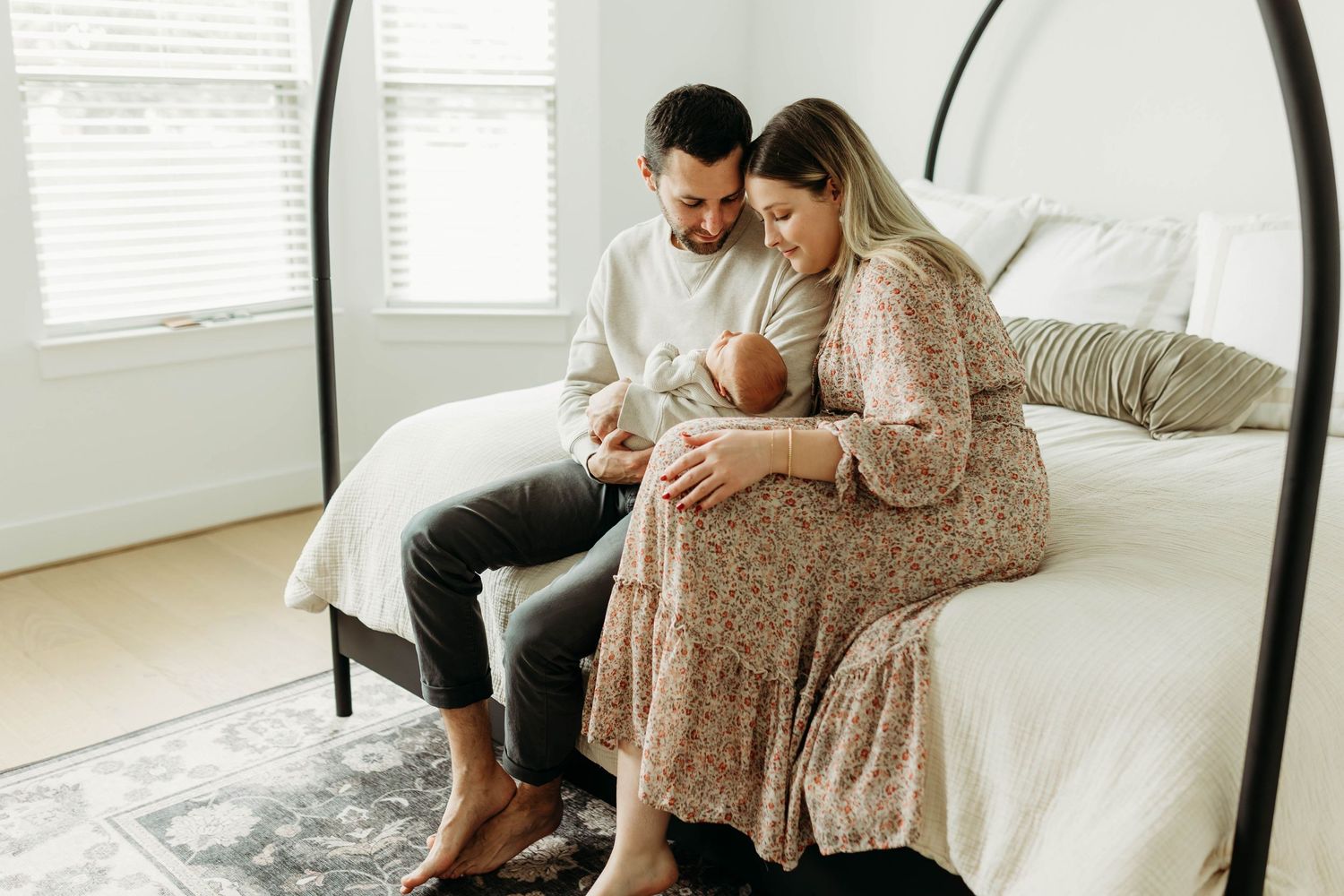 New parents sitting on bed with arched headboard, lovingly looking down at their newborn.