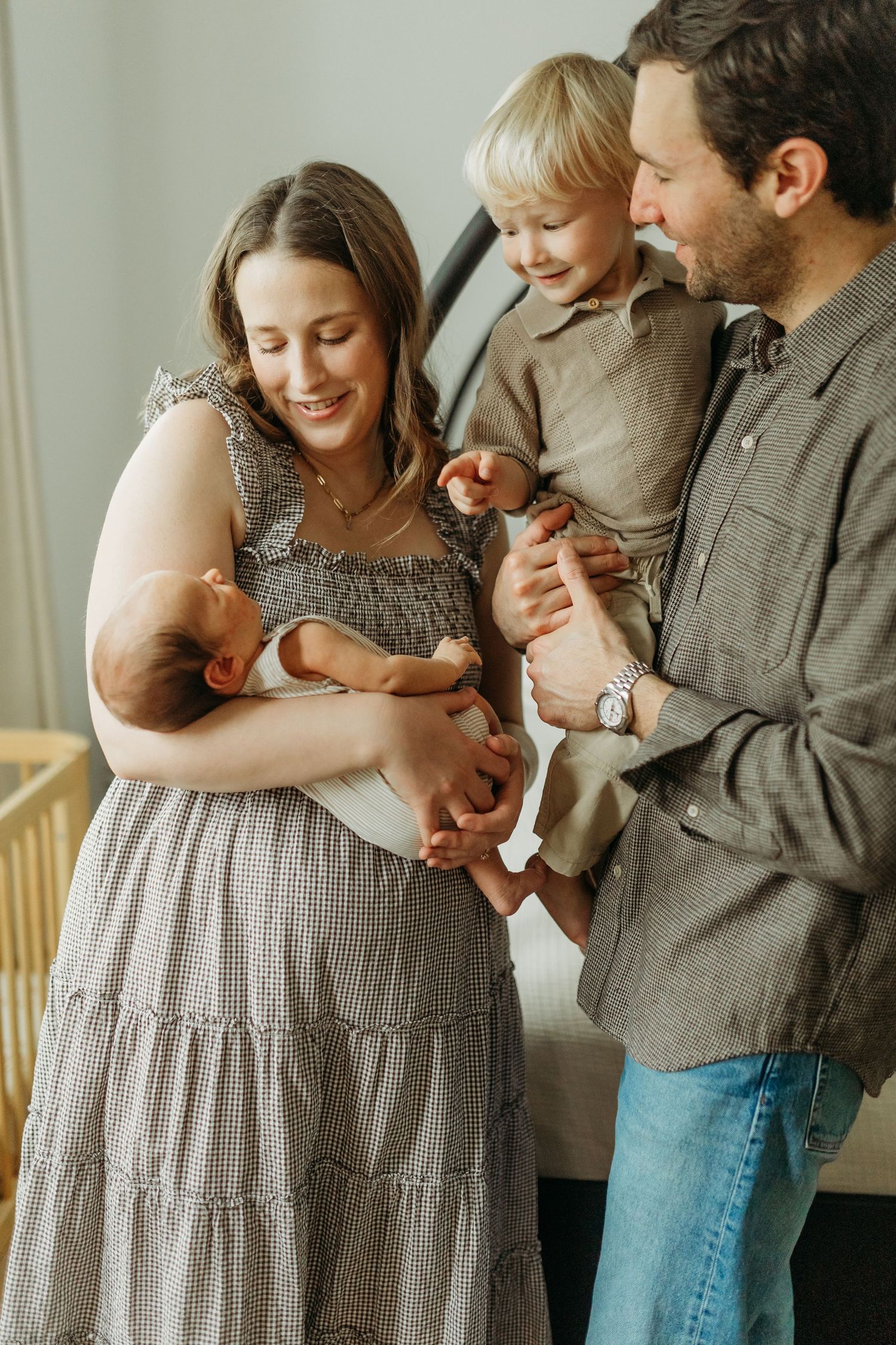 Parents smiling lovingly at their toddler and newborn baby during an intimate indoor family portrait session.