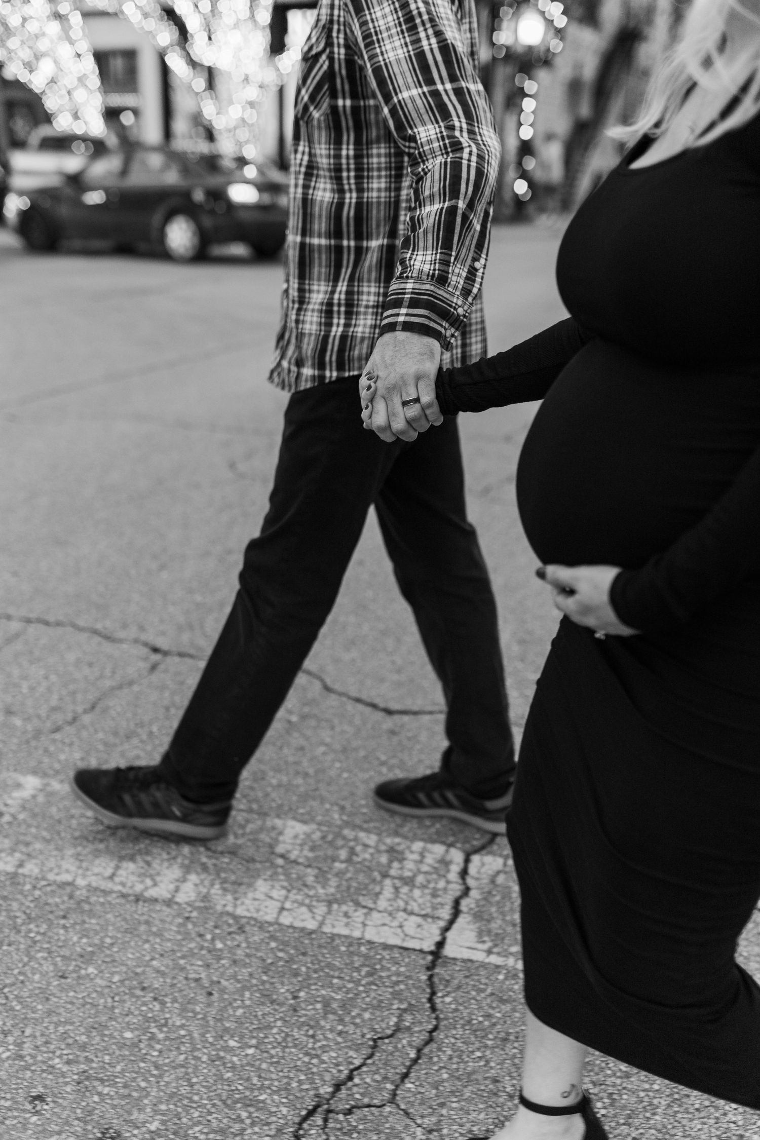 Black and white photo of pregnant couple holding hands while walking on a city street.