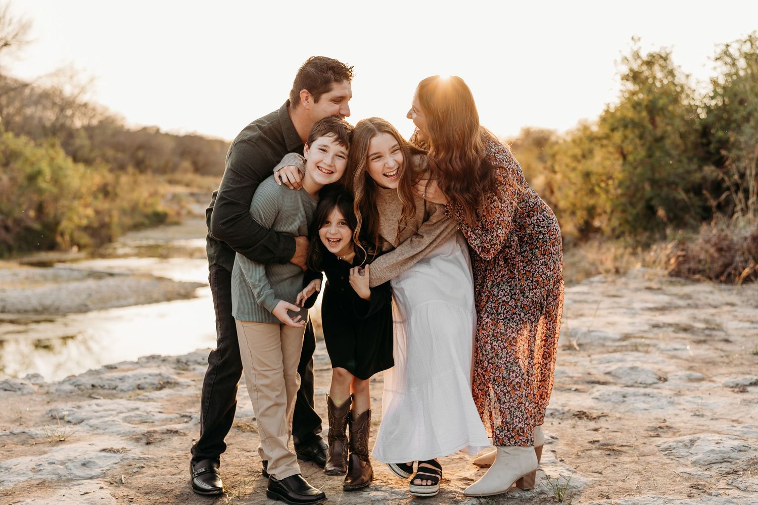Family of five posing together near a creek surrounded by autumn foliage at sunset.