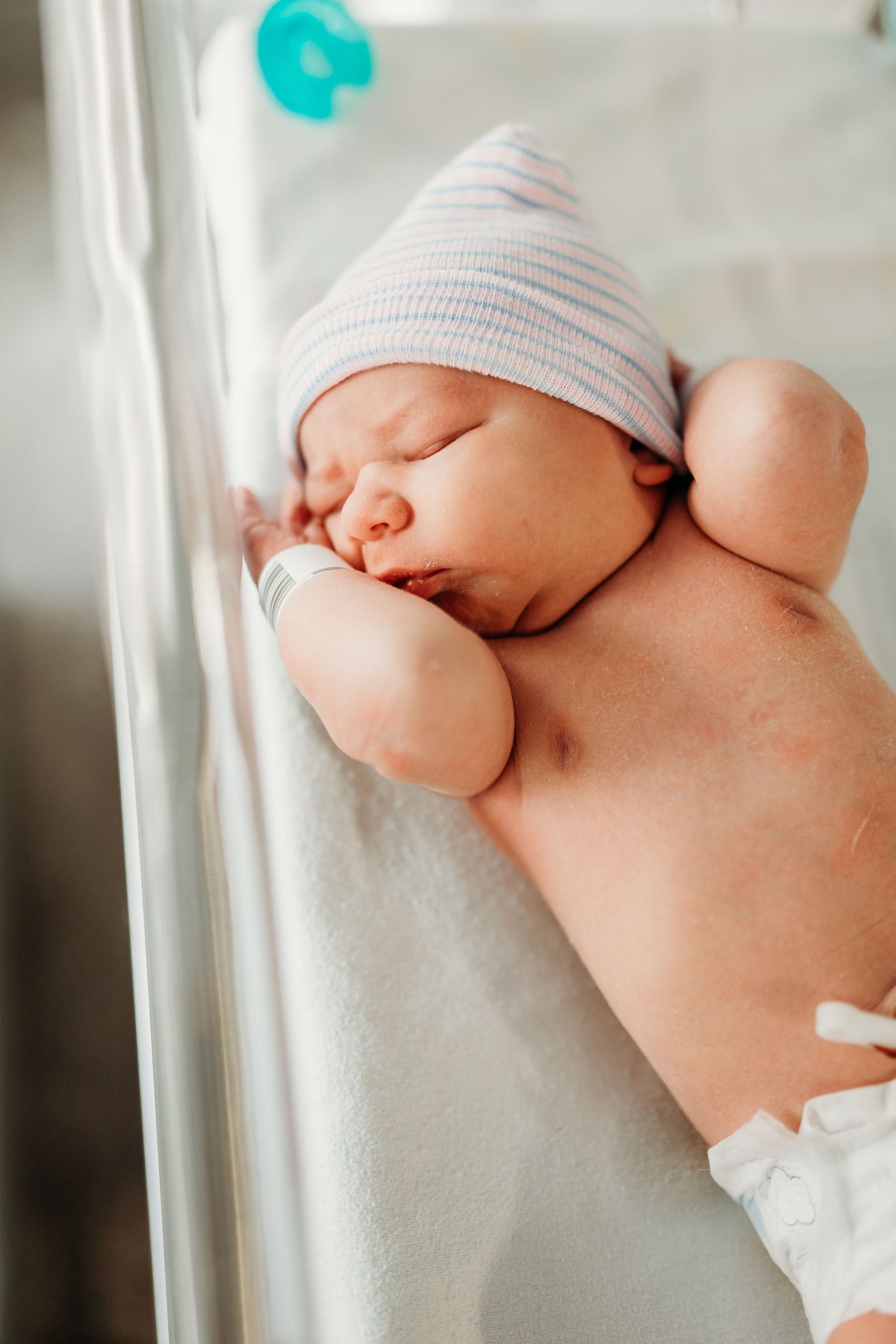A peaceful newborn baby sleeps in a hospital bassinet wearing a striped hat shortly after birth.