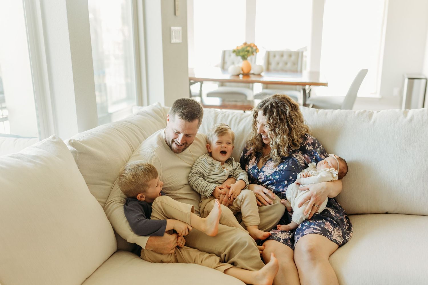 Happy family with three young children and newborn baby cuddling on a cream sofa.