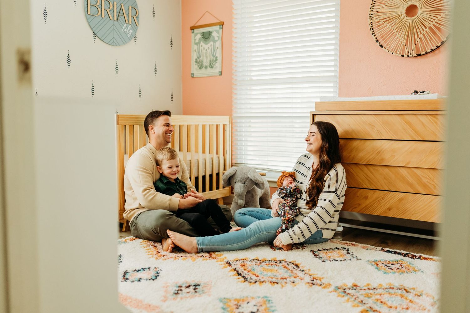 A happy family sits on a nursery floor, sharing a joyful moment with their newborn.