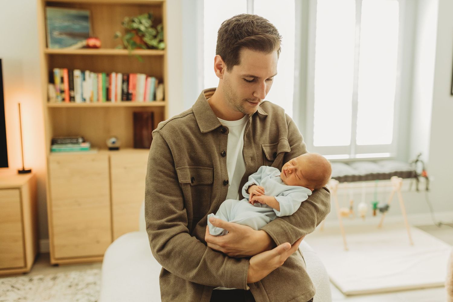 Young father cradling sleeping newborn baby in arms in modern home interior.