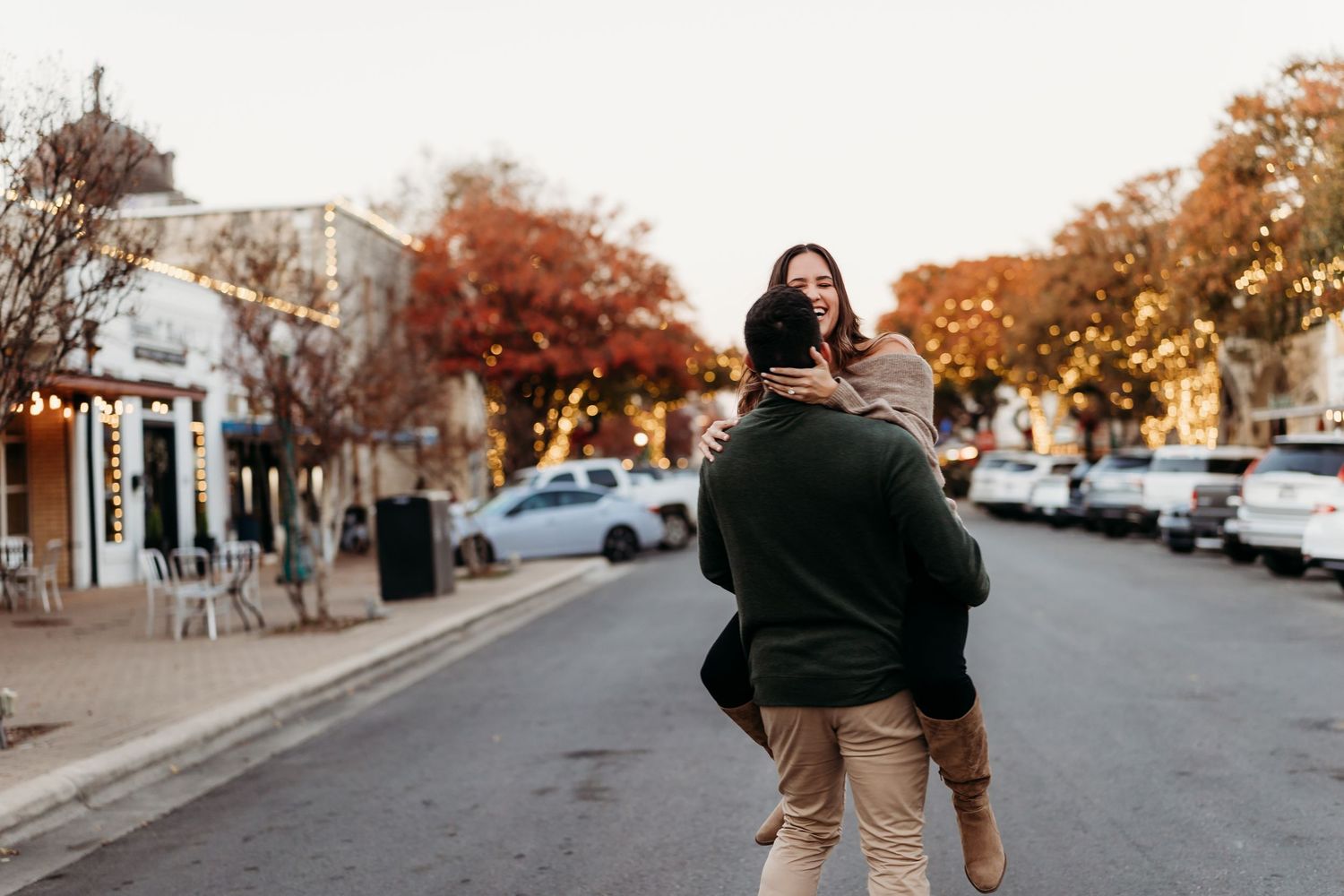 Couple sharing joyful hug in autumn street with colorful fall trees and warm bokeh lights.