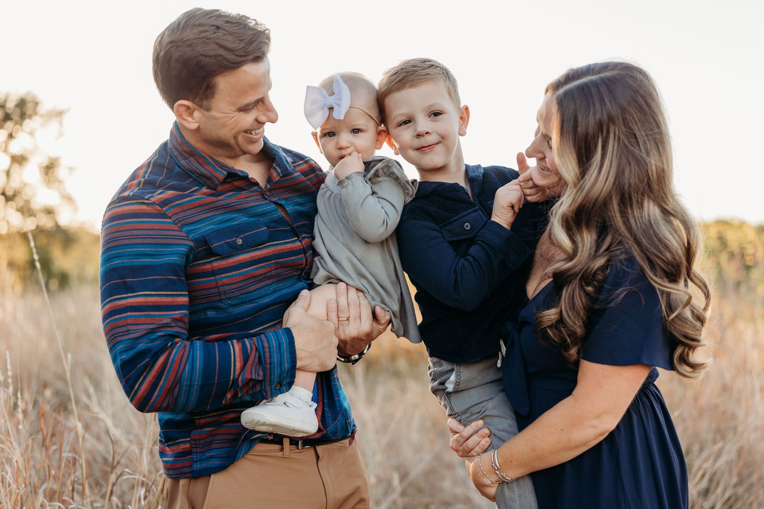 Happy family of four laughing together in a golden field during sunset photo session.
