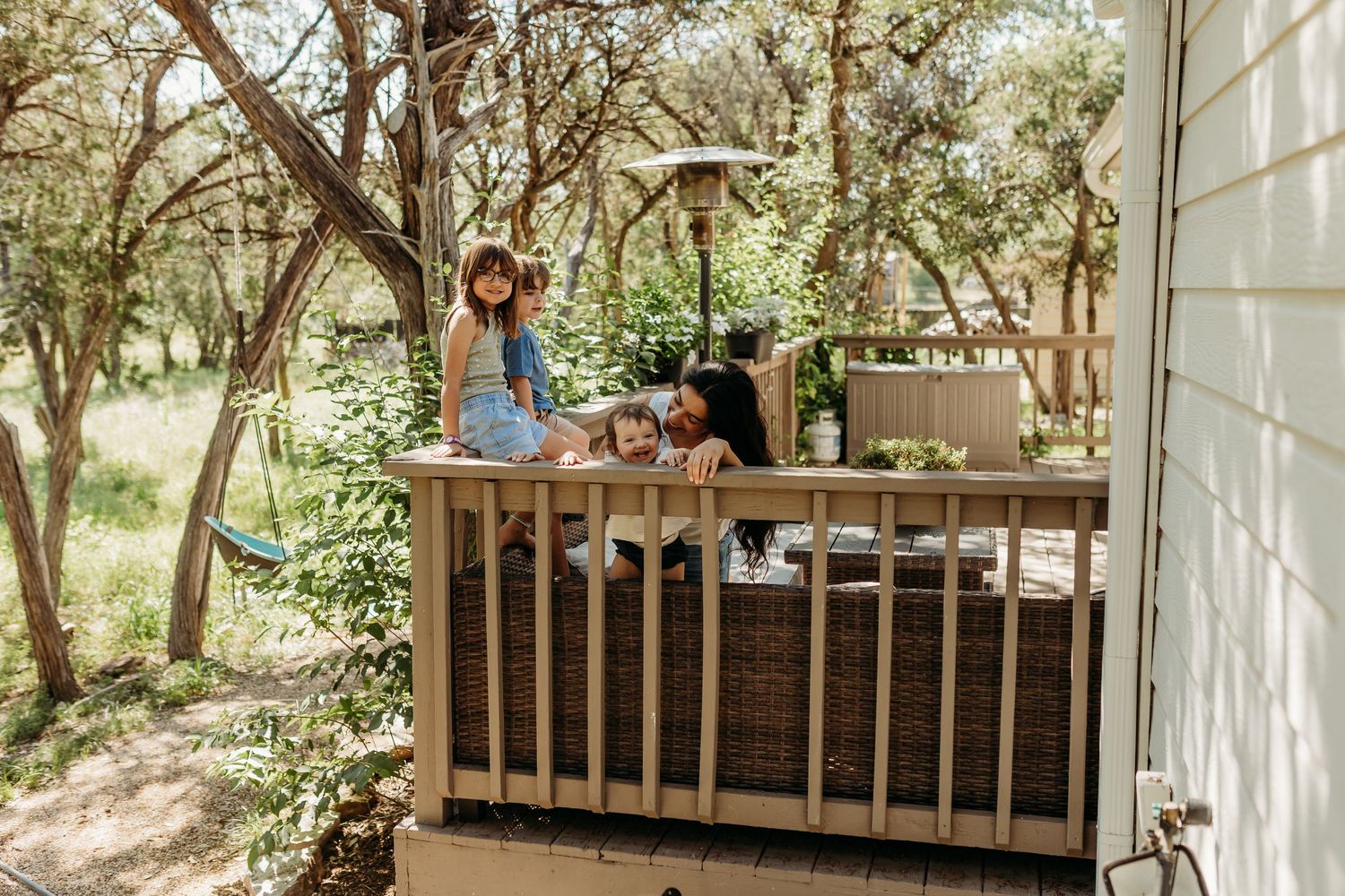 A family relaxes together on a wooden deck surrounded by lush green trees on a sunny day.