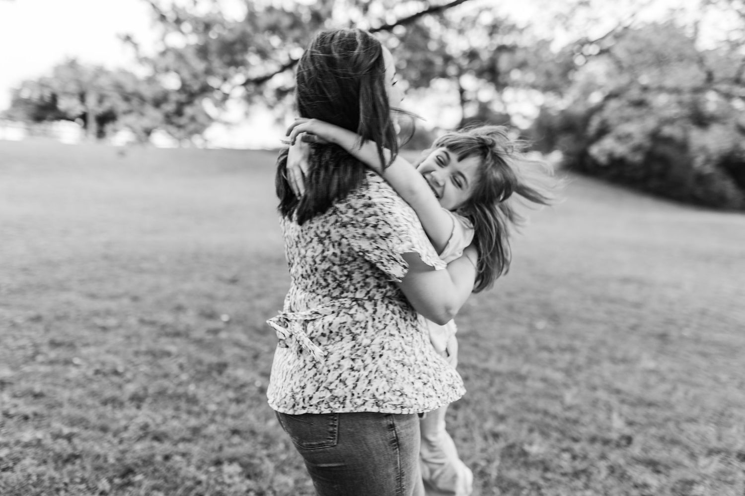 Two girls share a warm hug in a grassy park in a black and white photo.